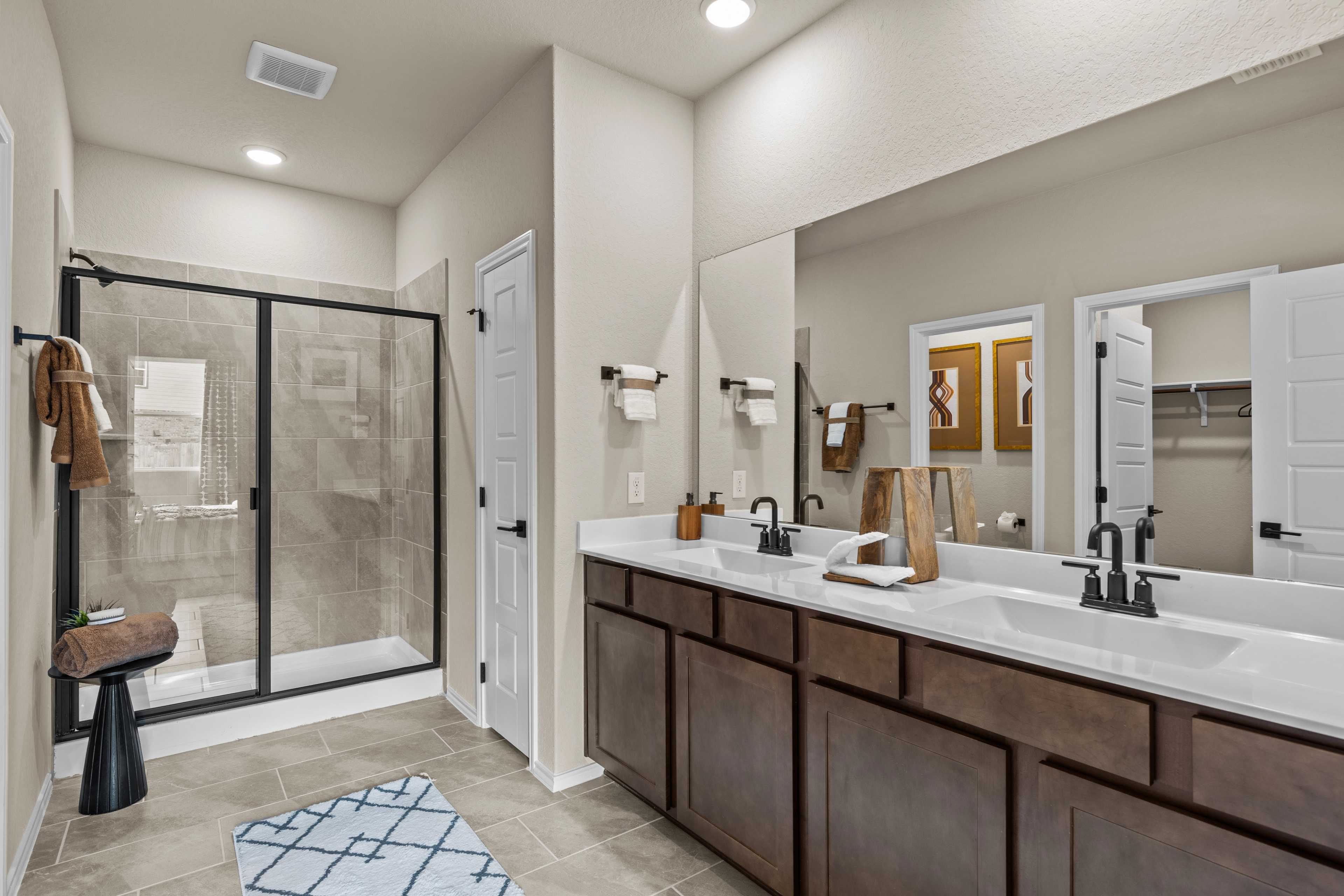 Modern master bathroom at Bricewood in San Antonio TX with double vanity, glass walk-in shower, and wood cabinets by Davidson Homes