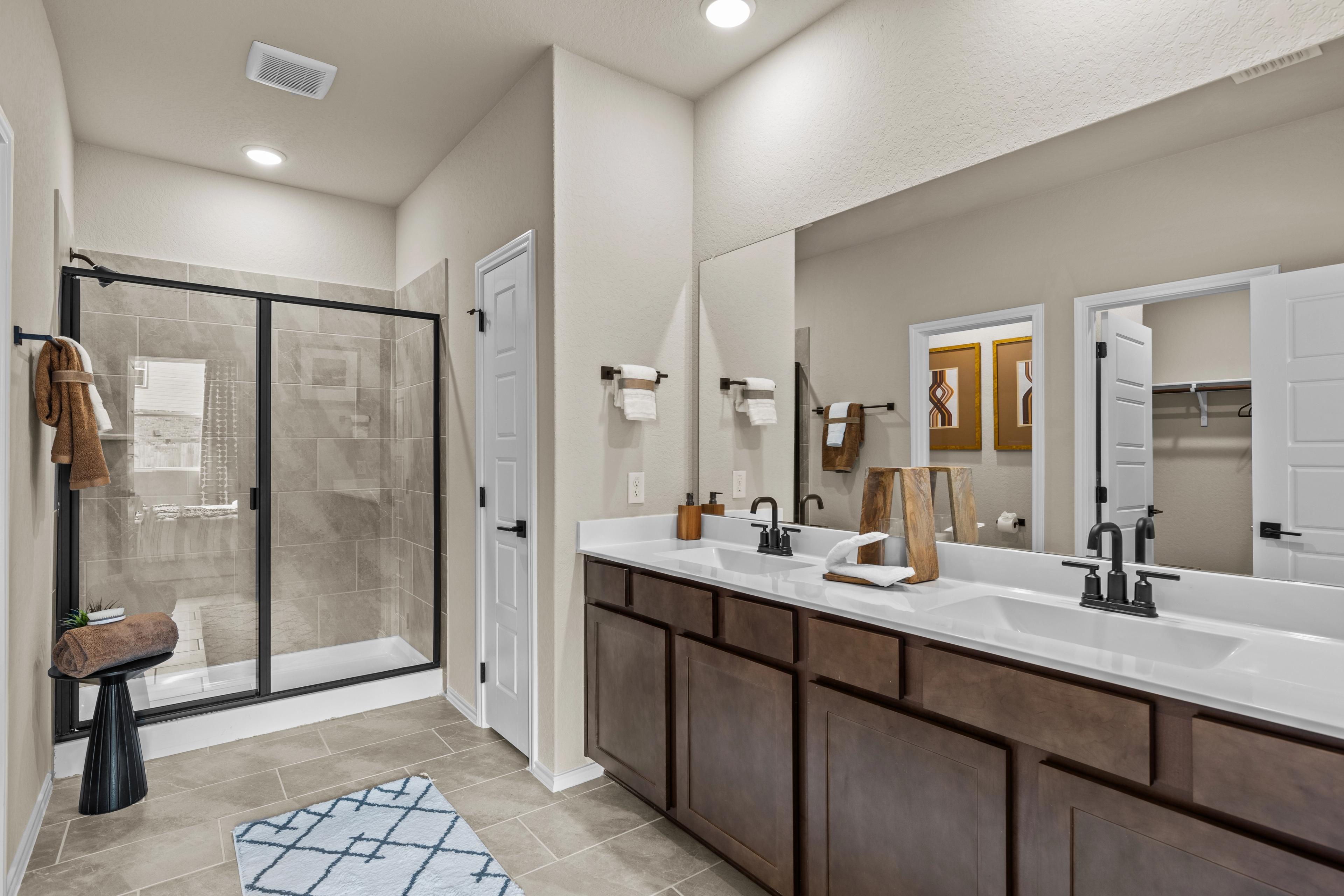 Modern master bathroom at Bricewood in San Antonio TX with double vanity, glass walk-in shower, and wood cabinets by Davidson Homes