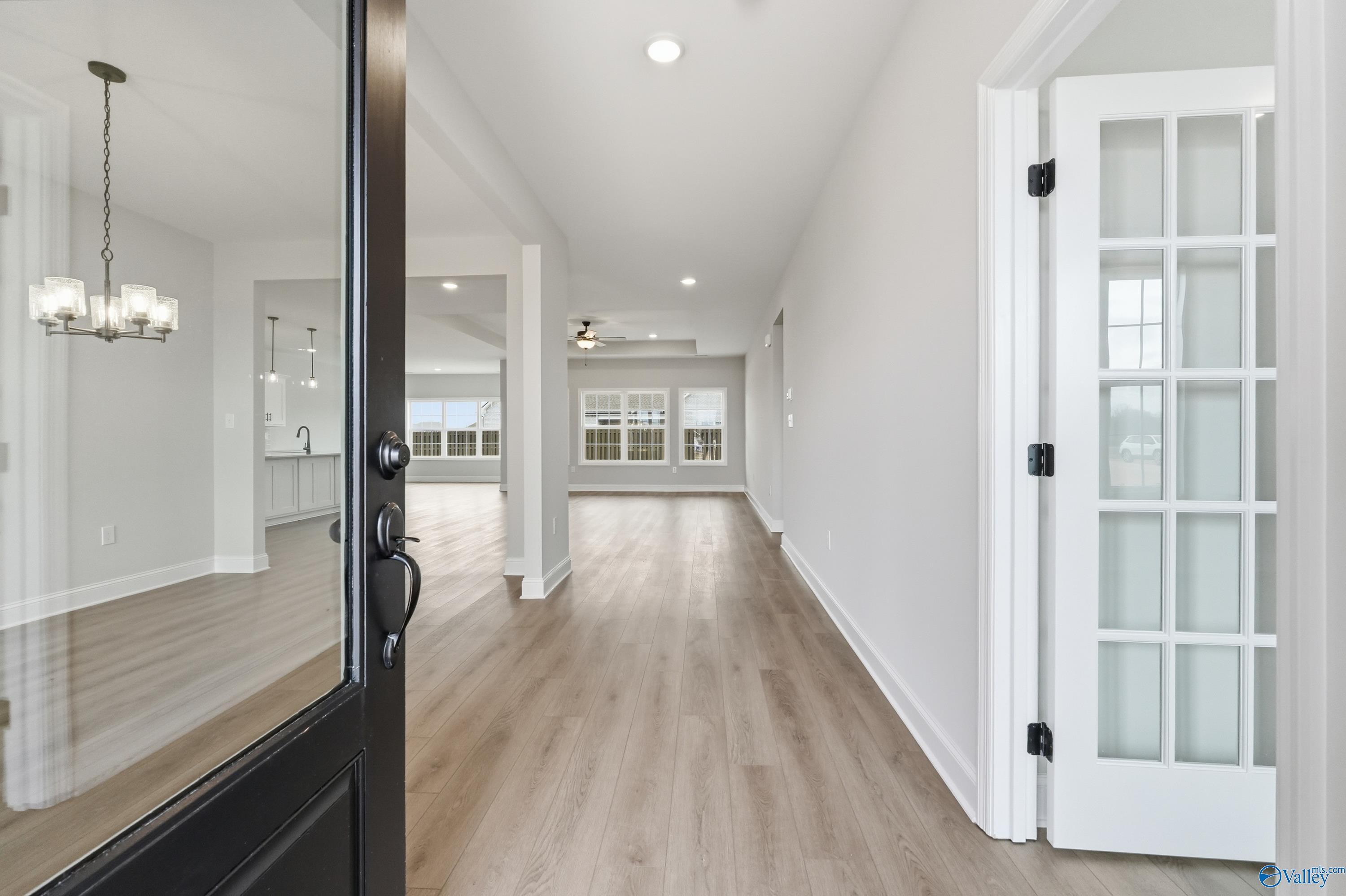 Bright entryway with open black door, light oak floors, chandelier, and kitchen view in The Finleigh home, Meridianville, Alabama