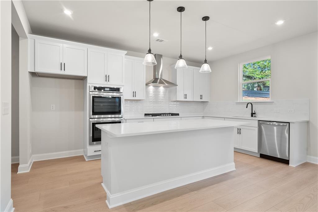 Modern white kitchen with quartz island, stainless steel appliances, and pendant lights in Davidson Homes The Hickory E, Buford, GA
