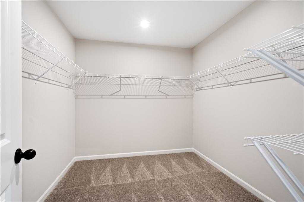 Spacious walk-in closet with white wire shelving and beige carpeted floor in Davidson Homes The Marion A, Kennesaw, GA
