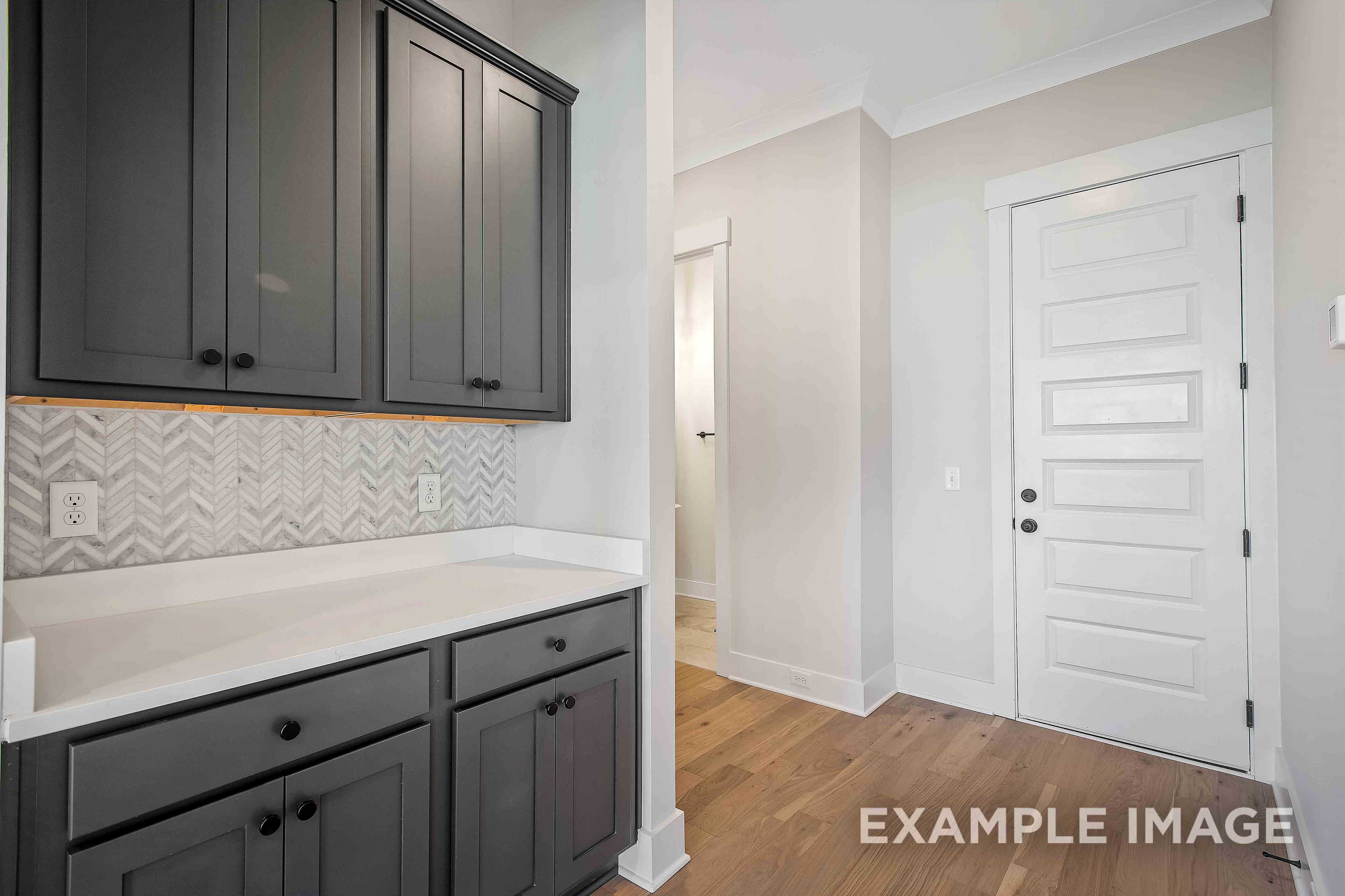 Modern kitchen in The Alston A featuring dark gray shaker cabinets, herringbone backsplash, white counters, and adjacent powder room