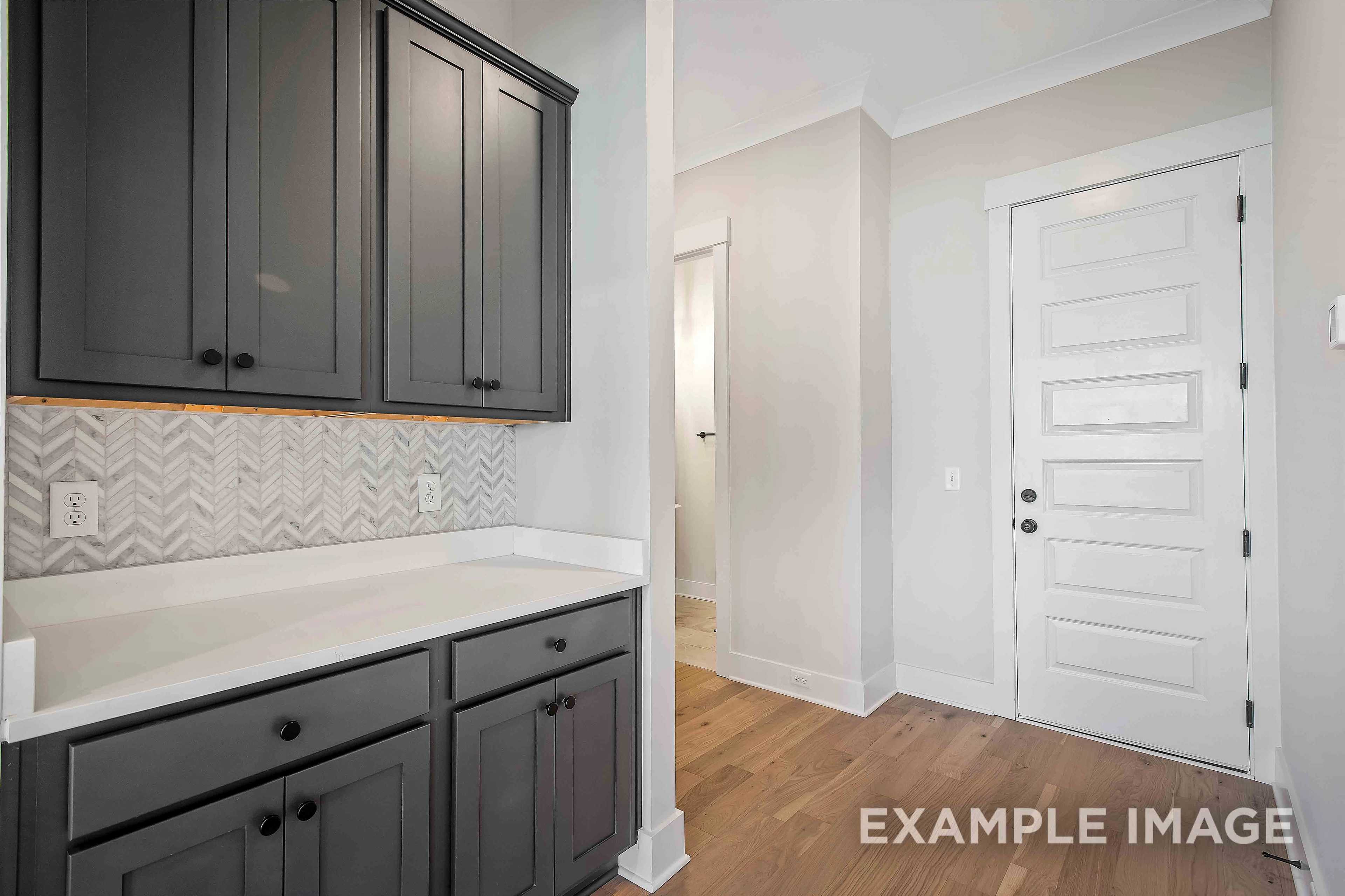 Modern kitchen in The Alston A featuring dark gray shaker cabinets, herringbone backsplash, white counters, and adjacent powder room