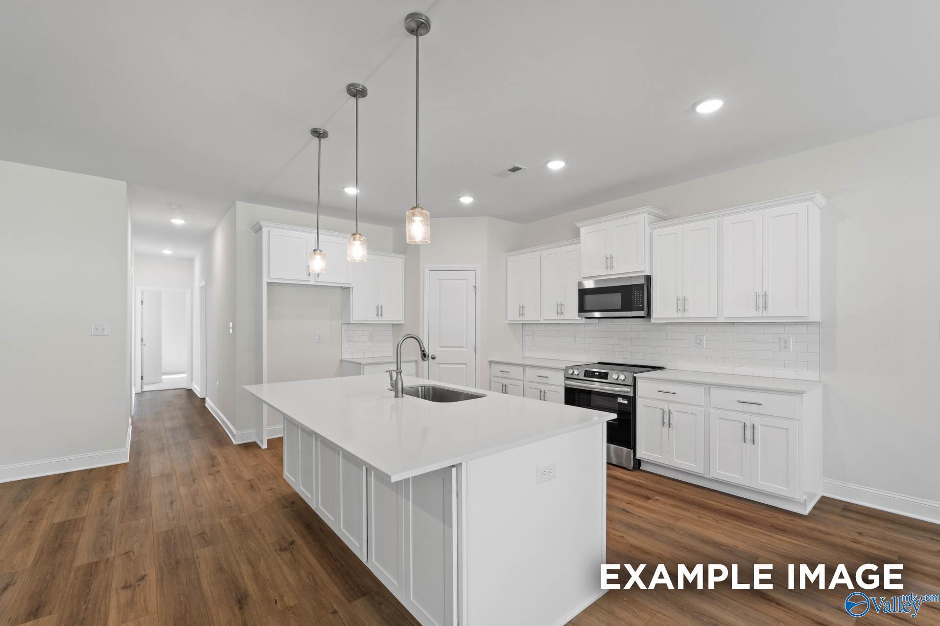 Modern white kitchen with large island sink, stainless appliances, pendant lights in Davidson Homes Rockford C, Madison AL