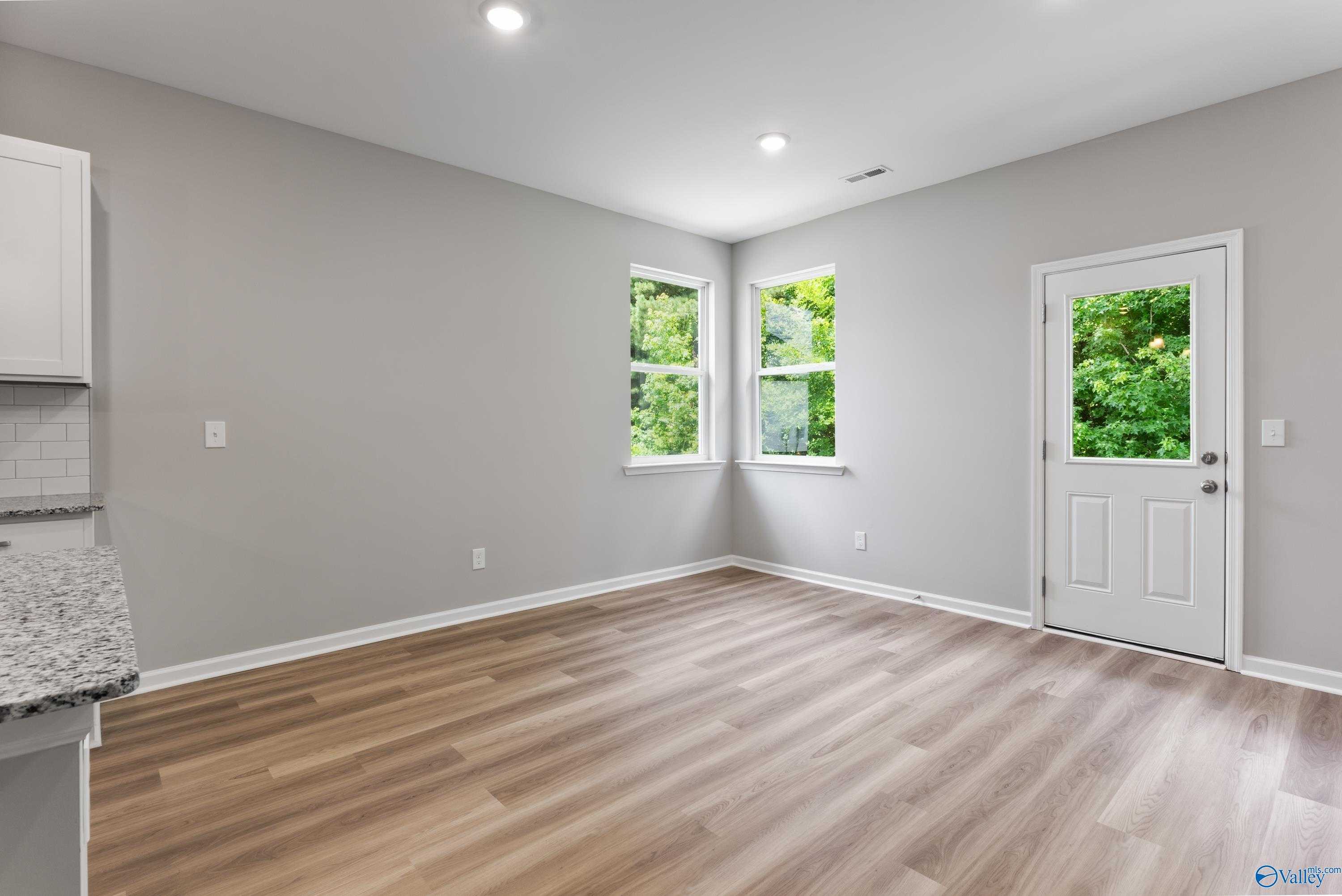 Bright kitchen with white cabinets, granite counters, subway tile backsplash, and hardwood floors opening to green patio view in Davidson Homes The Phoenix, Hazel Green, Alabama