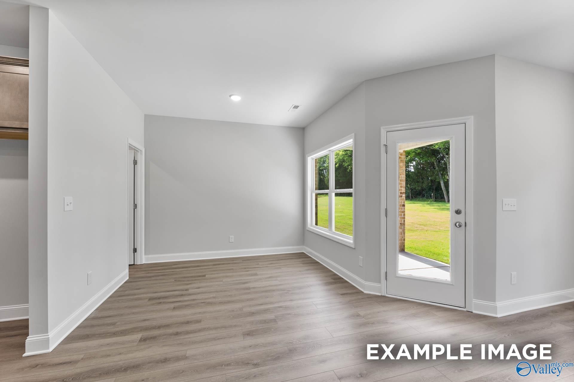 Bright living room with gray walls, wood floors, large windows, and French doors to green backyard in Davidson Homes The Daphne C, Arab, Alabama