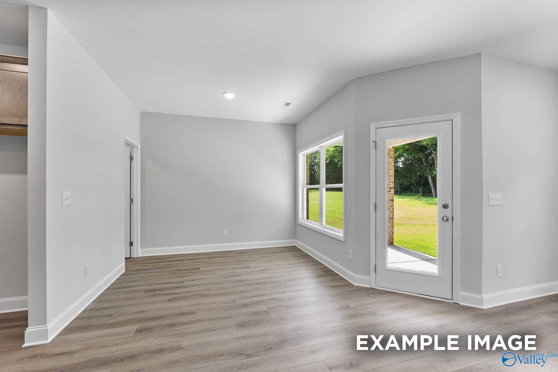 Bright living room with gray walls, wood floors, large windows, and French doors to green backyard in Davidson Homes The Daphne C, Arab, Alabama