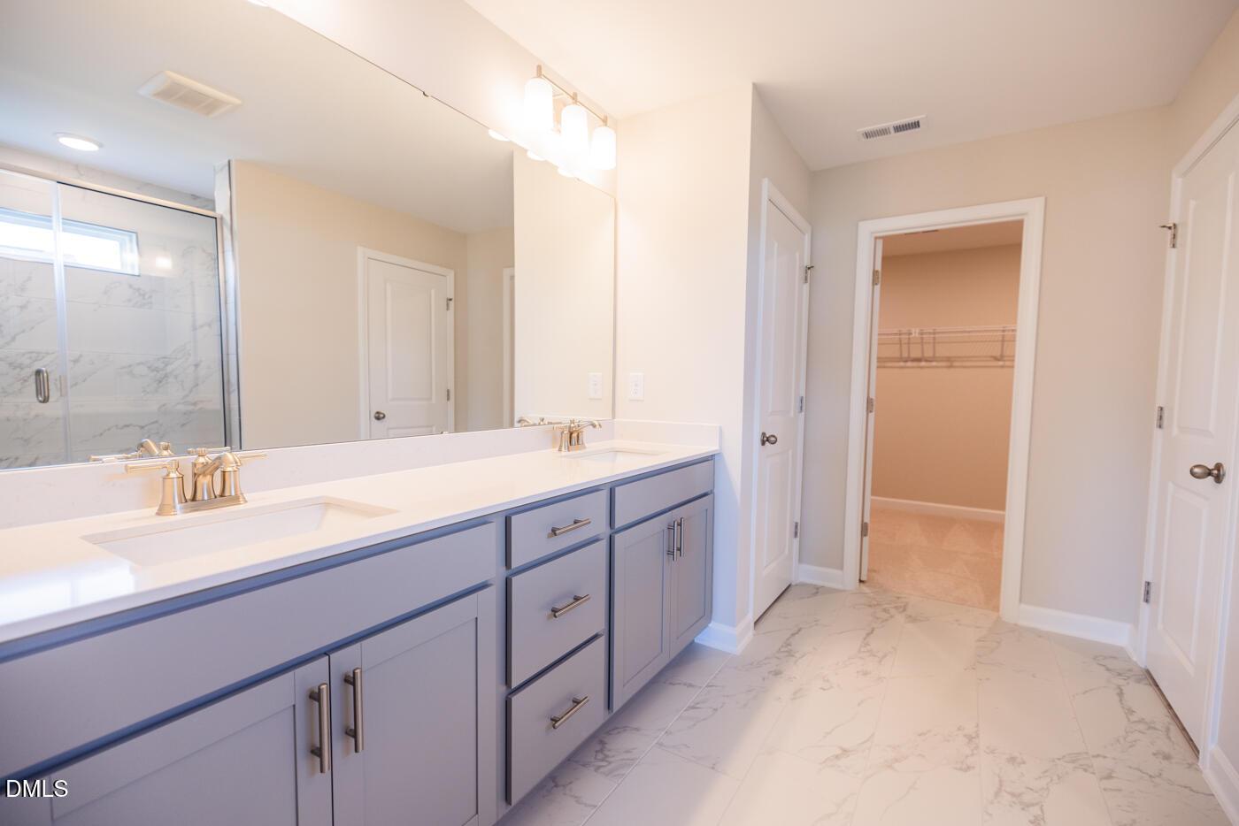 Modern master bathroom with double vanity, blue cabinets, frameless glass shower, and walk-in closet in Davidson Homes Hickory II C, Zebulon, NC