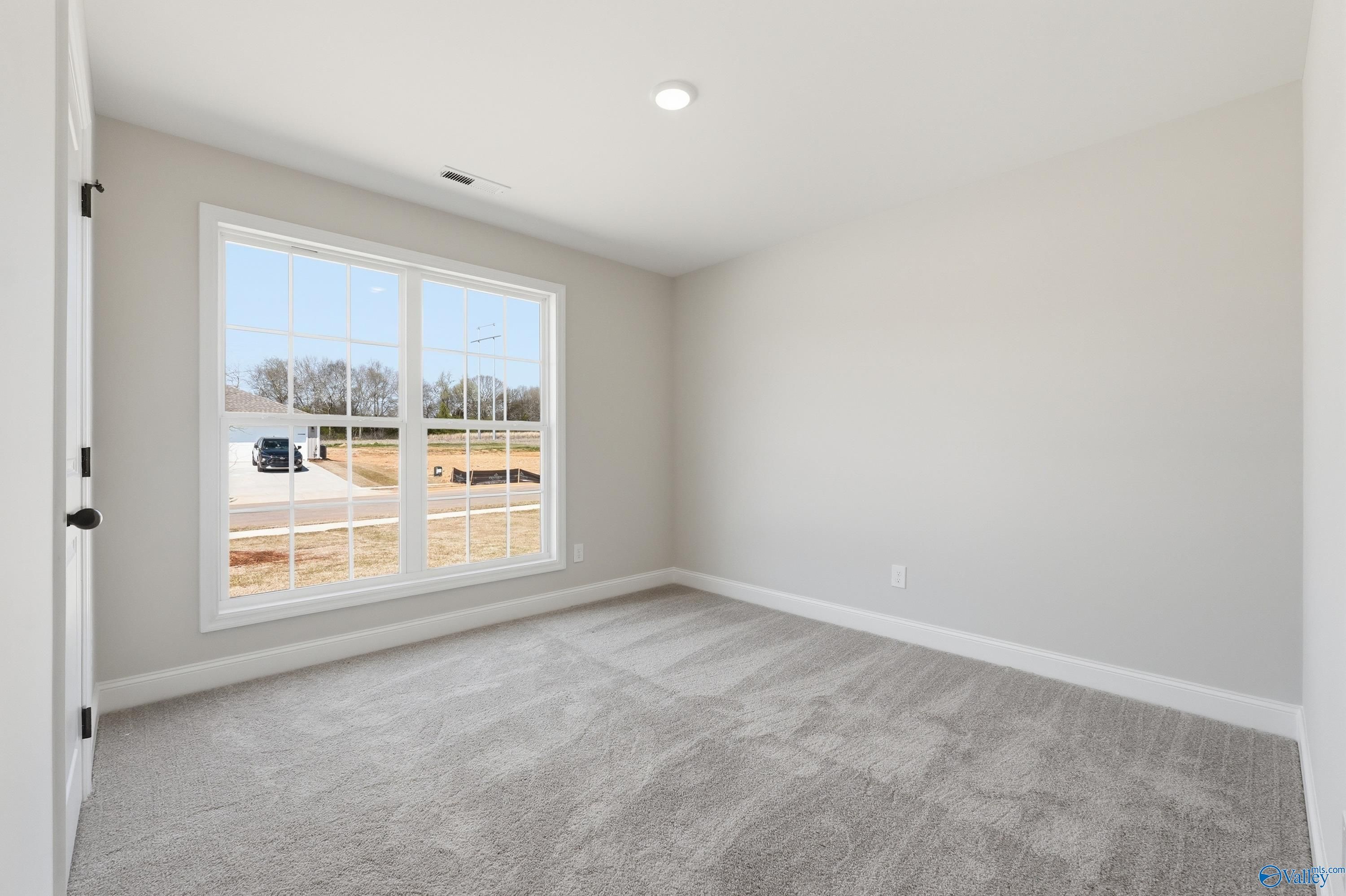 Bright secondary bedroom with gray carpet, light walls, and large window overlooking new construction in The Franklin V, Athens, Alabama