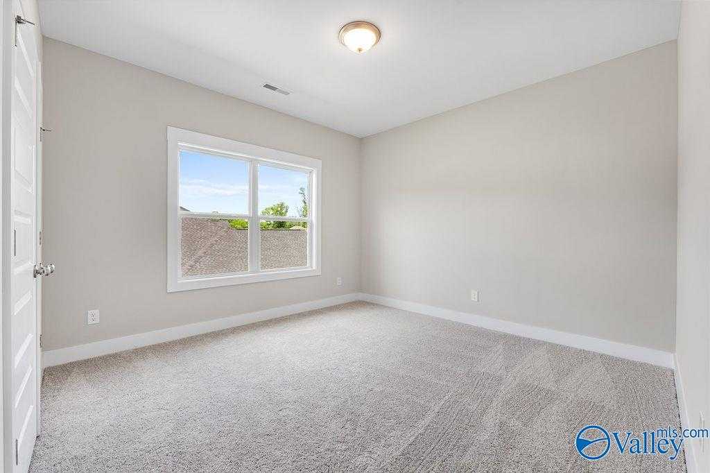 Bright empty bedroom with beige walls, carpeted floor, and large window overlooking greenery in Evermore Homes The Oxford, Owens Cross Roads, AL