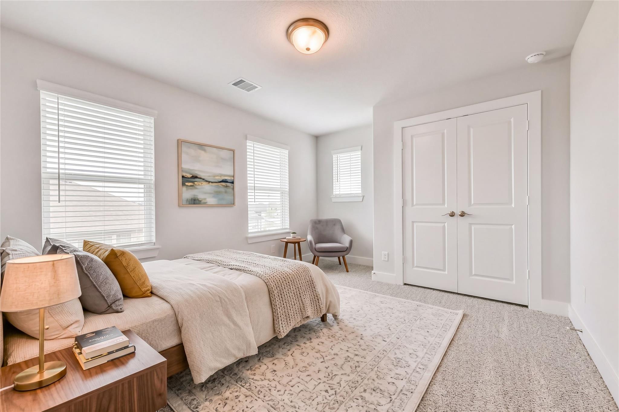 Serene secondary bedroom with neutral bedding, gray accent chair, seascape art, and double closet doors in Davidson Homes The Victoria A, Lago Mar