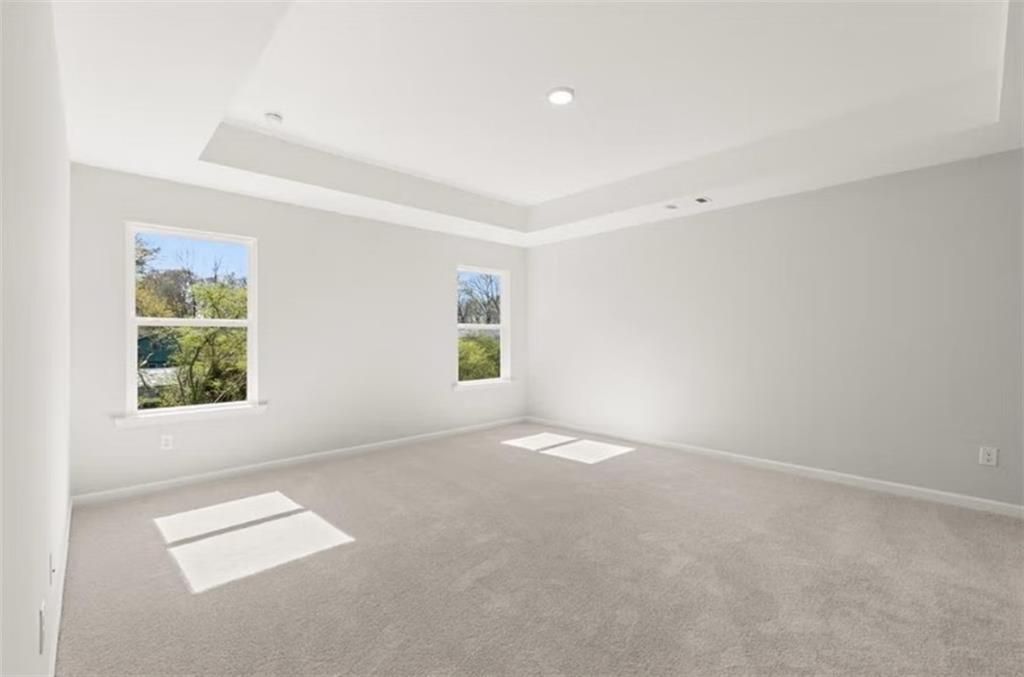 Bright secondary bedroom with light gray walls, gray carpet, tray ceiling, and large windows overlooking trees in The Hickory B, Winder, GA