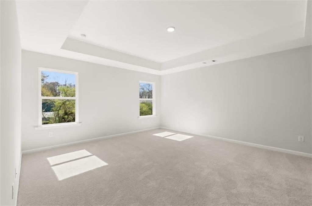 Bright secondary bedroom with light gray walls, gray carpet, tray ceiling, and large windows overlooking trees in The Hickory B, Winder, GA