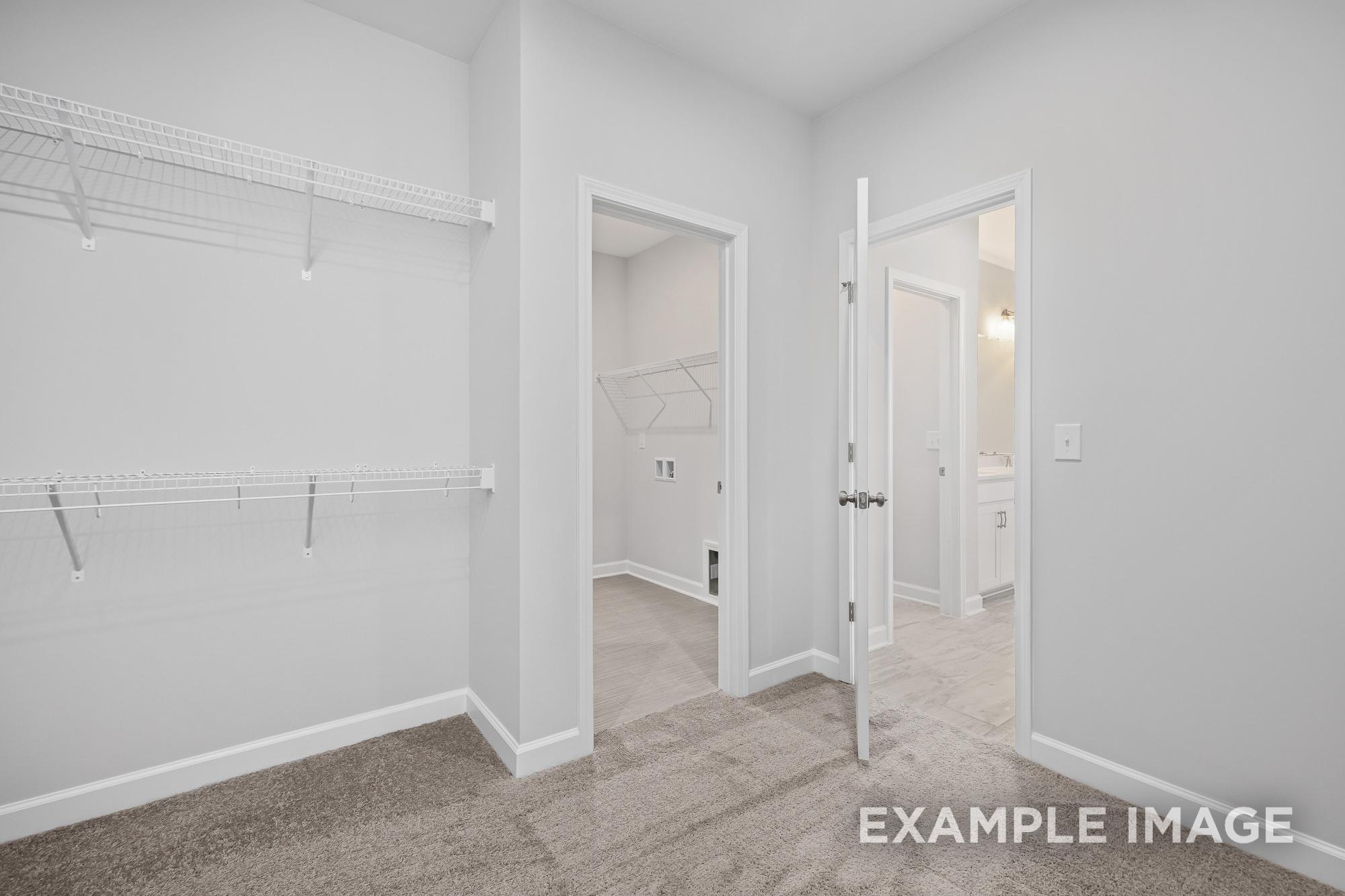 Spacious master walk-in closet in The Cypress B II with wire shelving, adjacent laundry room, and en-suite bathroom door