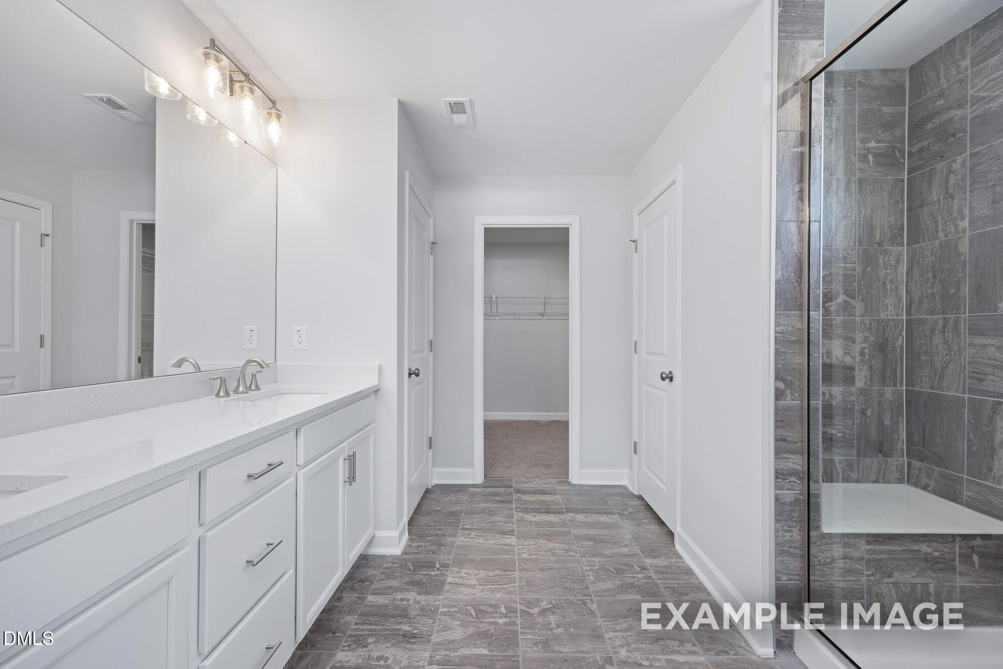 Modern master bathroom featuring double white vanity, frameless glass shower, and gray tile floor in Davidson Homes The Hickory II B, Lillington, NC