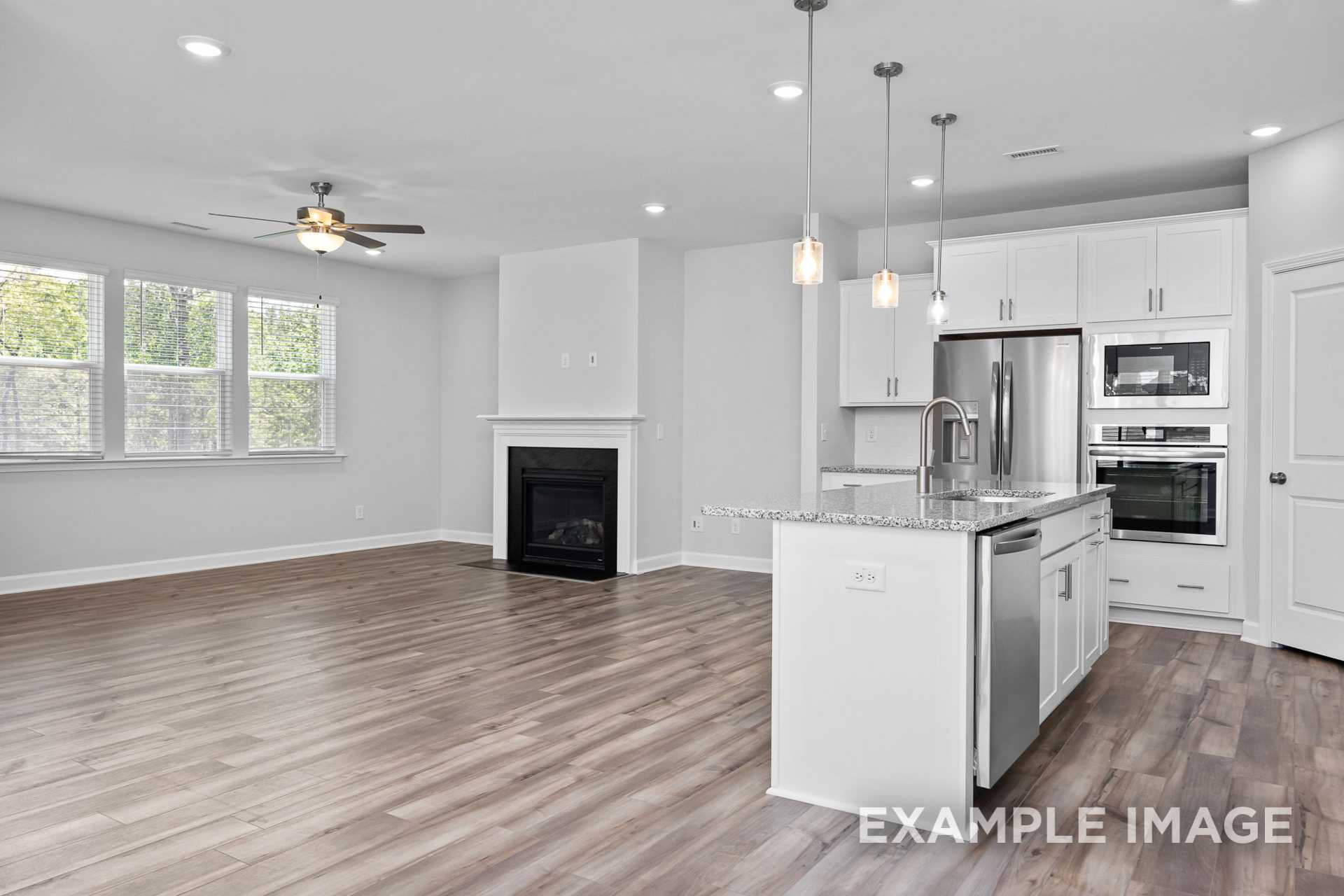 Open-concept kitchen and living area in The Preston B by Davidson Homes with white island, stainless appliances, fireplace, and hardwood floors