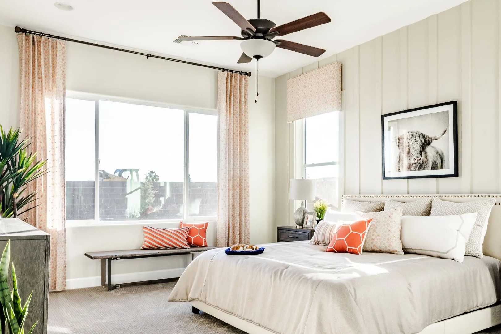 Spacious primary bedroom in Westwood Prescott AZ with beige walls, king bed, orange pillows, potted plants, and large sunny windows