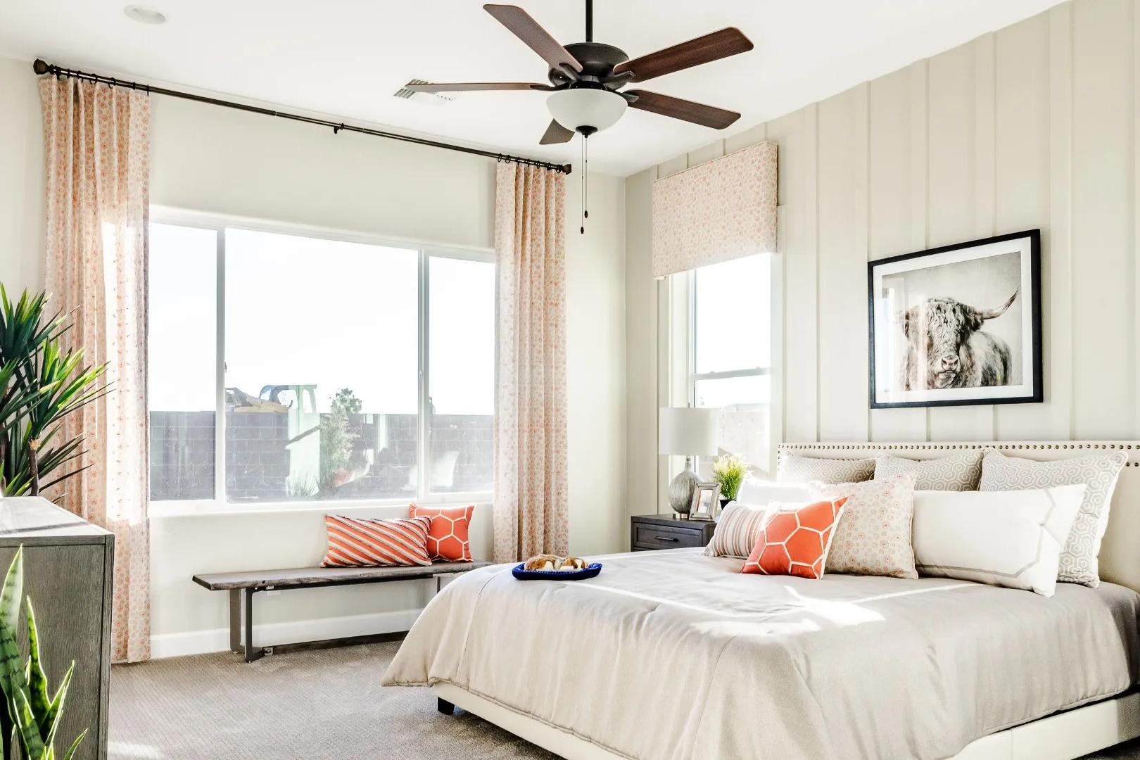 Spacious primary bedroom in Westwood Prescott AZ with beige walls, king bed, orange pillows, potted plants, and large sunny windows