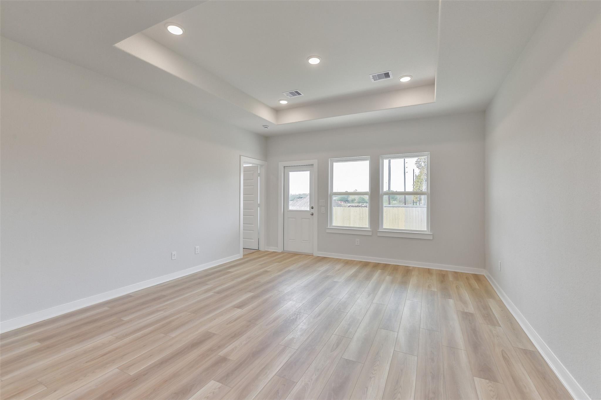 Bright living room with tray ceiling, recessed lights, large windows, French doors, and laminate flooring in Davidson Homes The Colorado G, Magnolia Texas