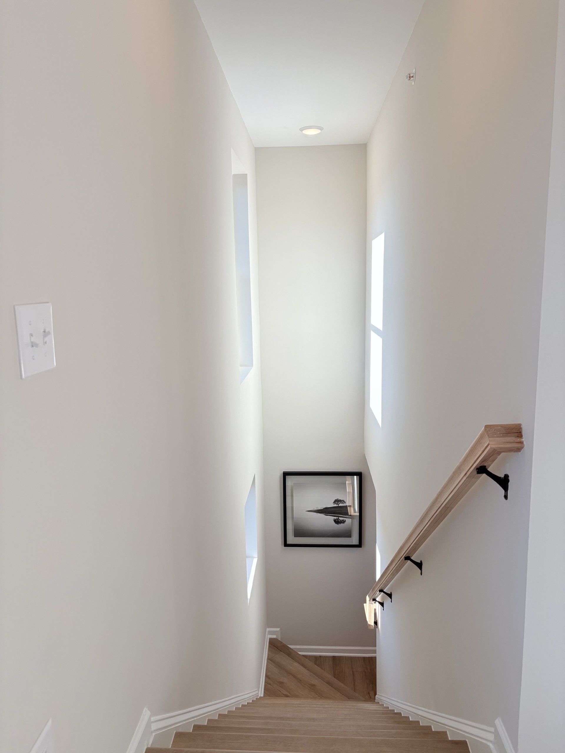 Elegant oak staircase with white walls, framed photo, and window in Hemingway home, Cumming GA by Davidson Homes