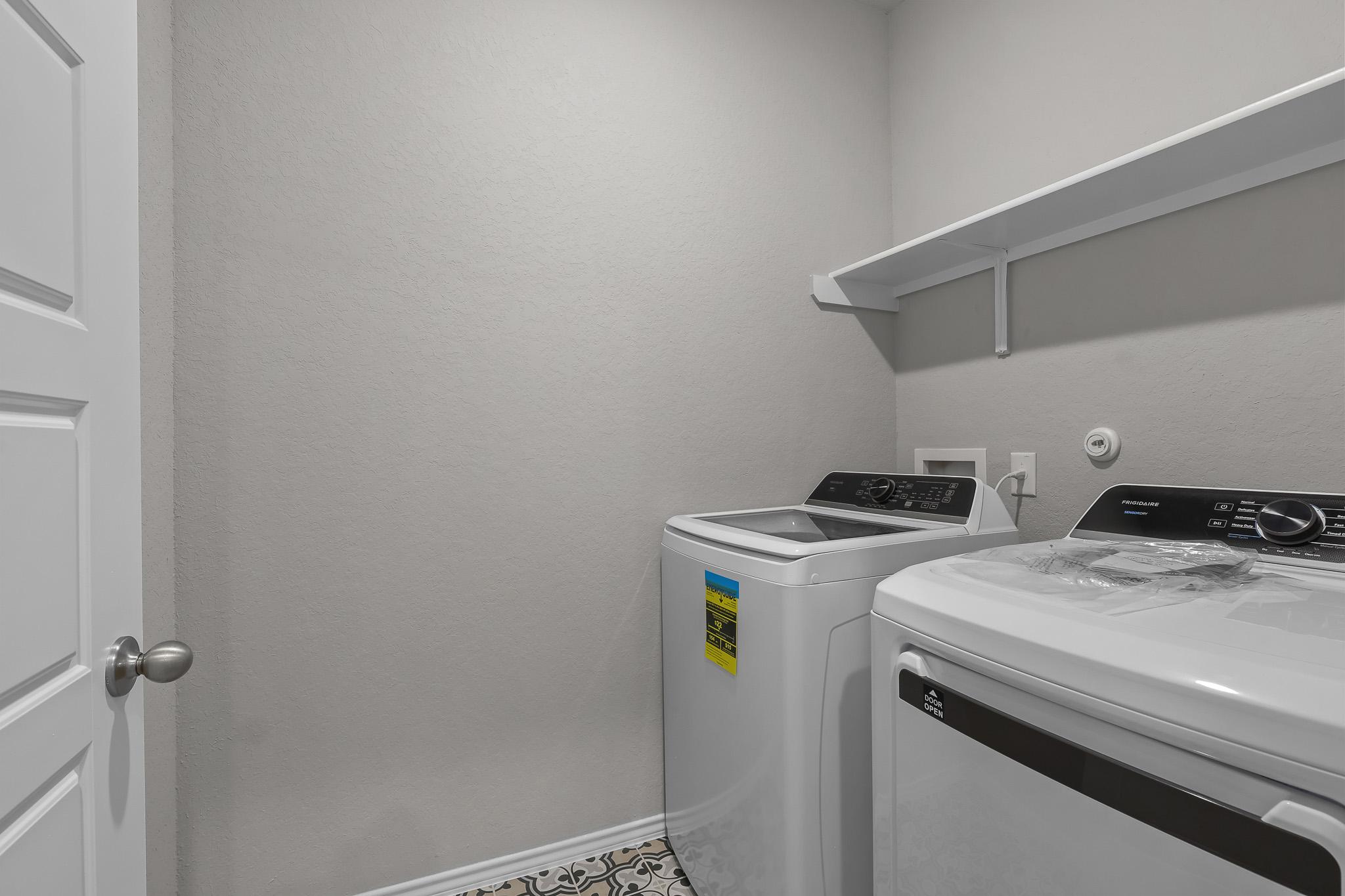 Laundry room in The Colorado B home design featuring white Frigidaire washer and dryer with overhead storage shelving.