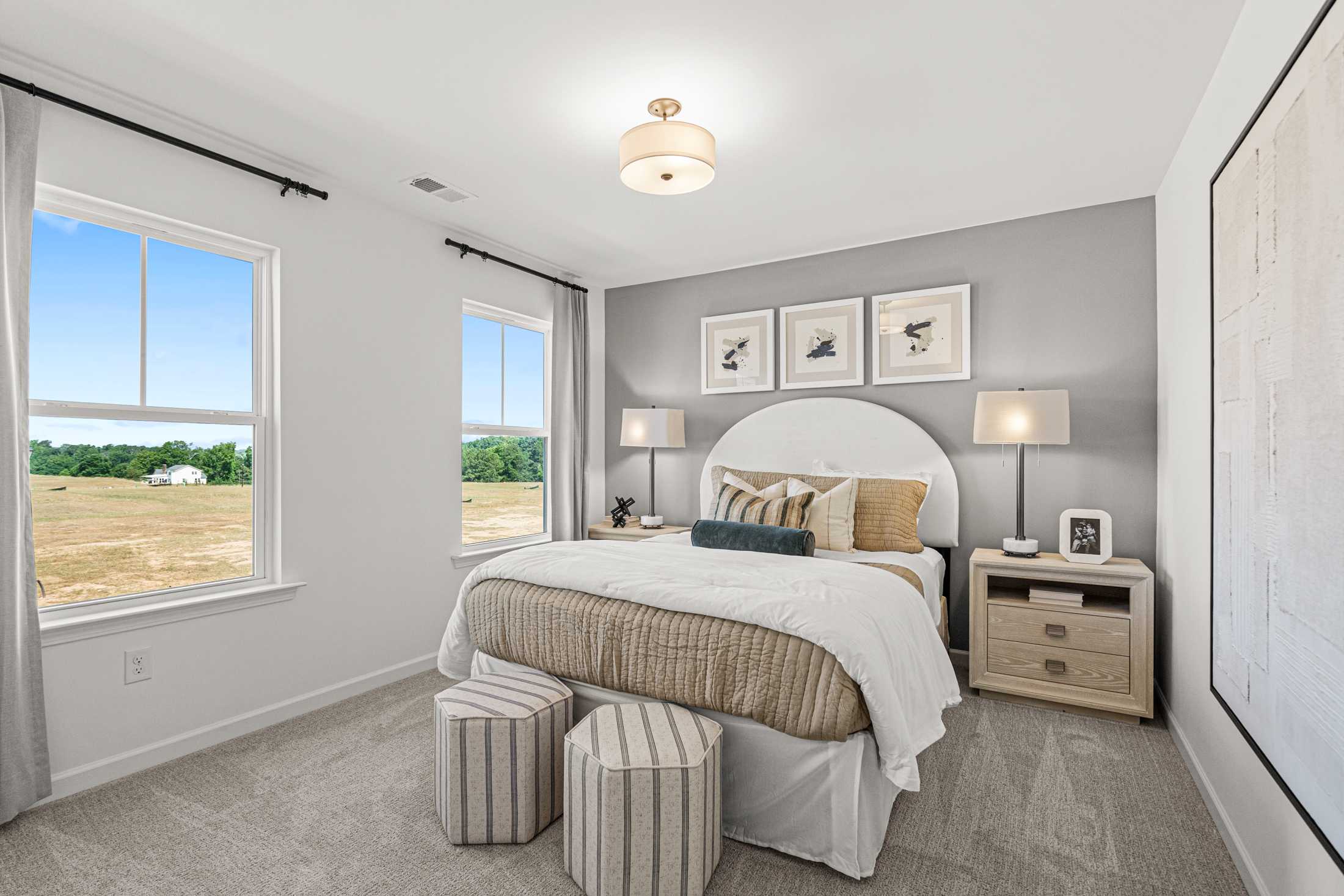 Cozy secondary bedroom in The Hickory A at Wehunt Meadows, light gray walls, beige bed with pillows, field view window, lamps and ottomans