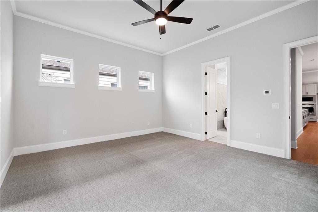 Spacious master bedroom with gray carpet, ceiling fan, three windows, and en-suite bath in Davidson Homes Seaside B, Woodstock, GA
