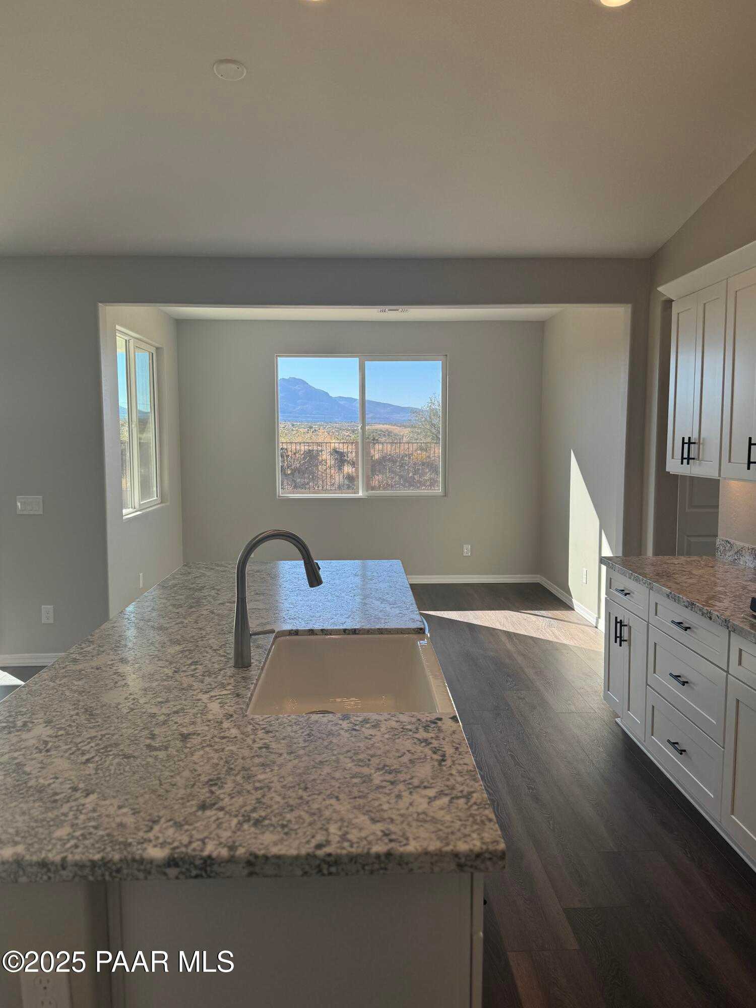 Modern kitchen island with granite countertop, farmhouse sink, white cabinets, and mountain view window in The Monarch E, Prescott, AZ