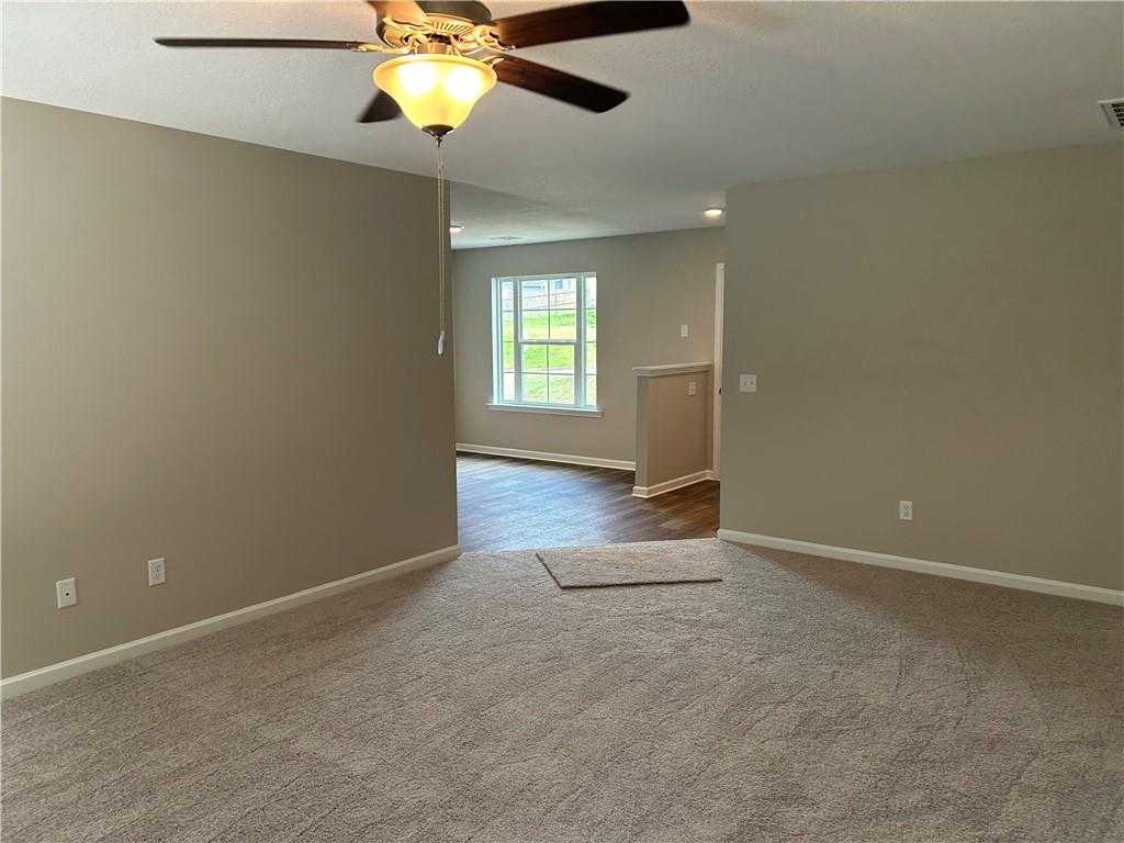 Empty living room with neutral beige walls, plush carpet, ceiling fan light, window overlooking green field in Davidson Homes The Washington, Phenix City, AL