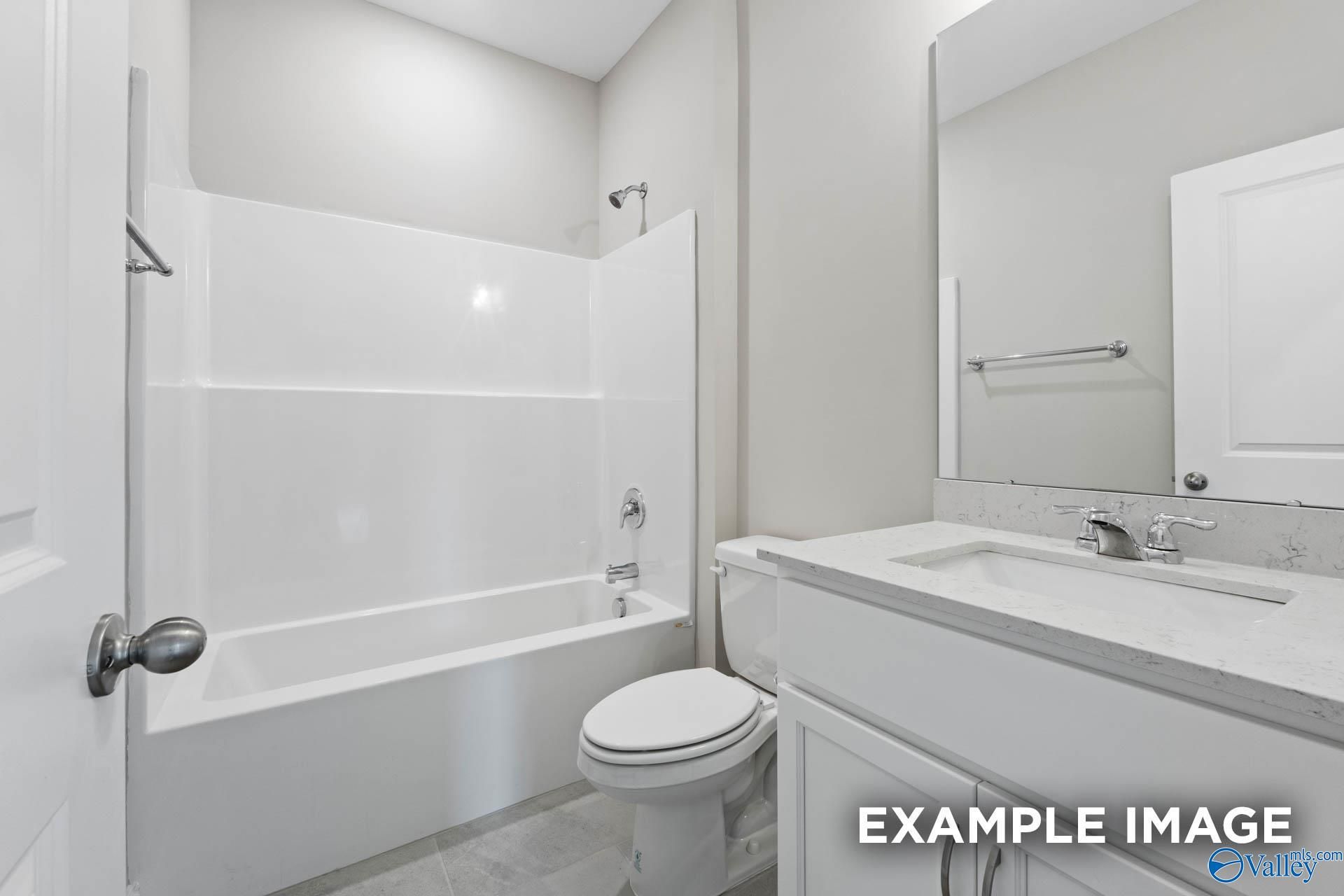 Modern bathroom with white tub-shower combo, quartz vanity sink, mirror, and tile floor in Davidson Homes The Montgomery, Meridianville, AL