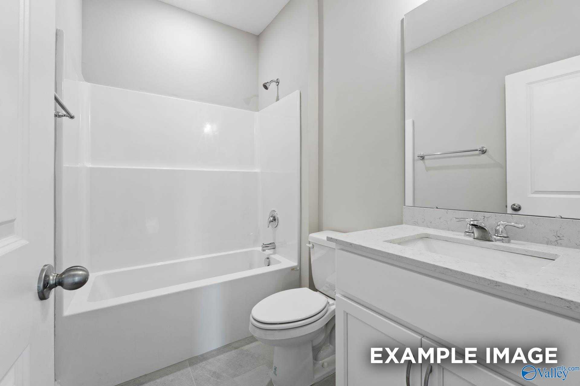 Modern bathroom with white tub-shower combo, quartz vanity sink, mirror, and tile floor in Davidson Homes The Montgomery, Meridianville, AL