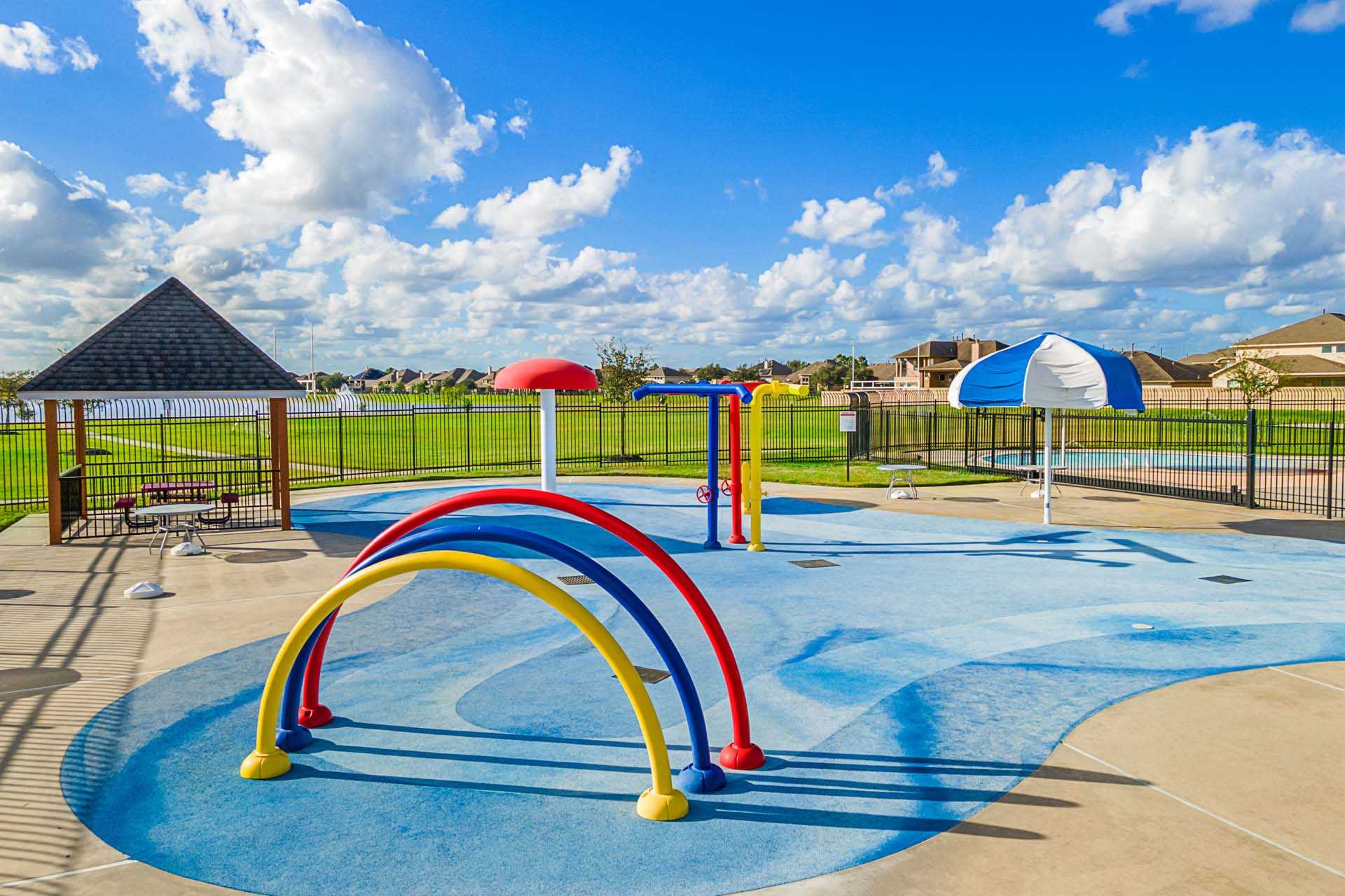 Colorful splash pad at Sierra Vista in Rosharon Texas with water arches umbrellas and shaded pavilion