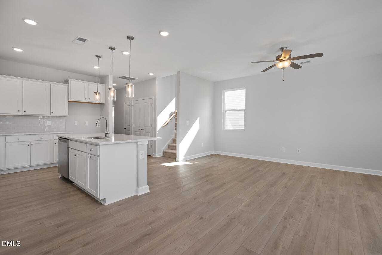 Open-concept kitchen with white cabinets, large island, hardwood floors, and ceiling fan in The Graham Exterior by Davidson Homes, Fuquay-Varina, NC