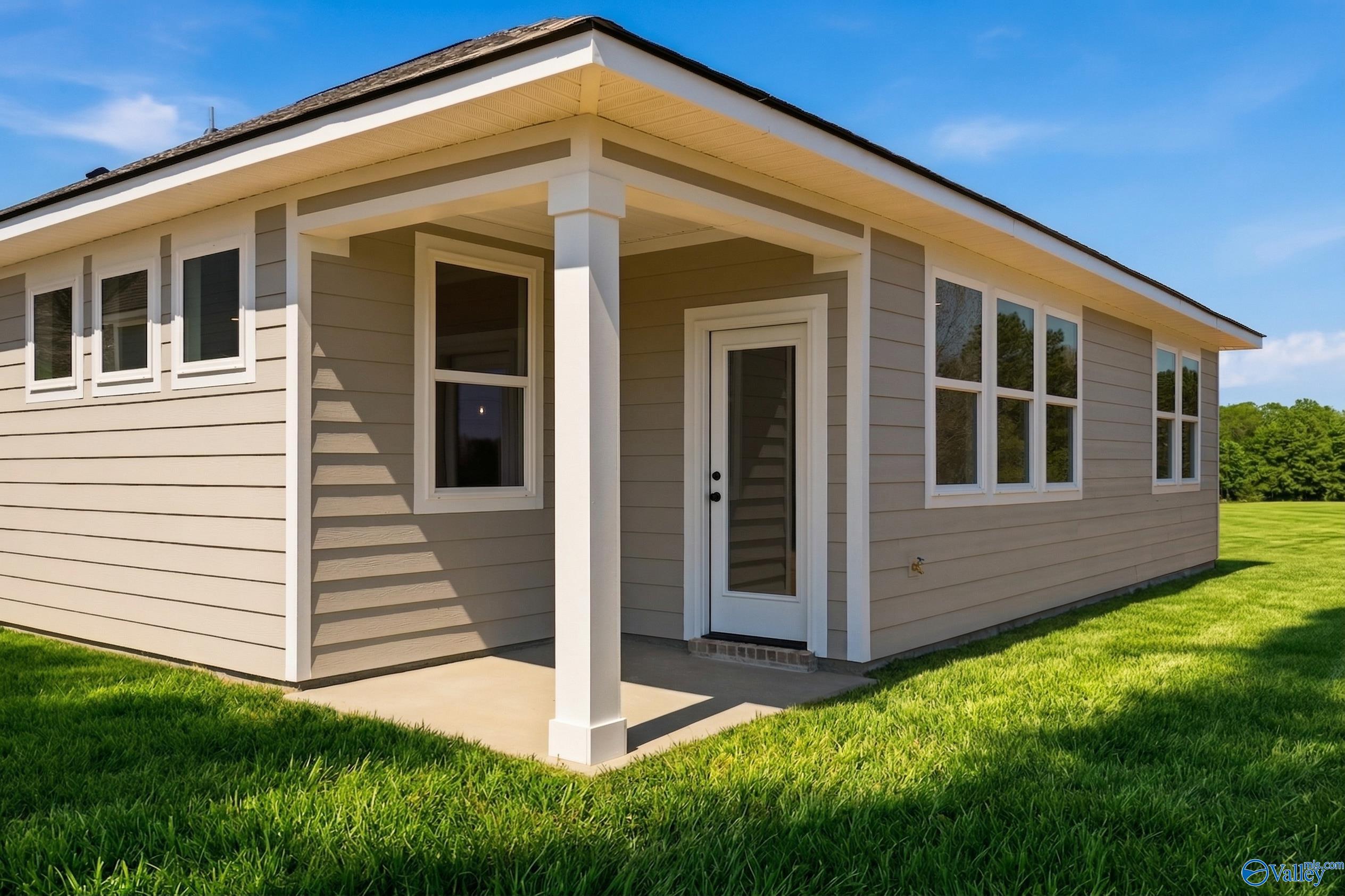 Tan single-story home with beige siding, covered porch, glass door, and large windows on green lawn in Noble Ridge, Cullman, Alabama