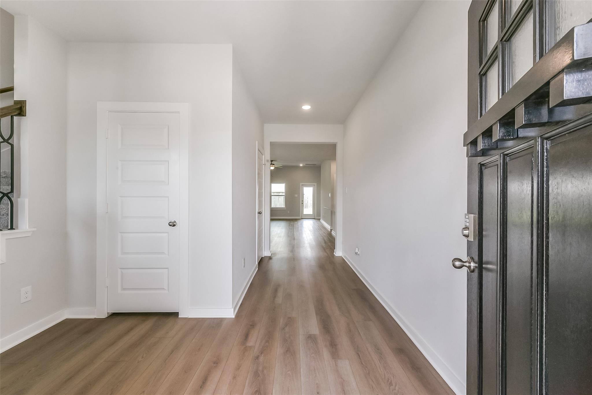 Expansive entry hallway with light wood laminate floors, white walls, and dark front door in Davidson Homes The Tierra C 4-bedroom, Dayton, Texas