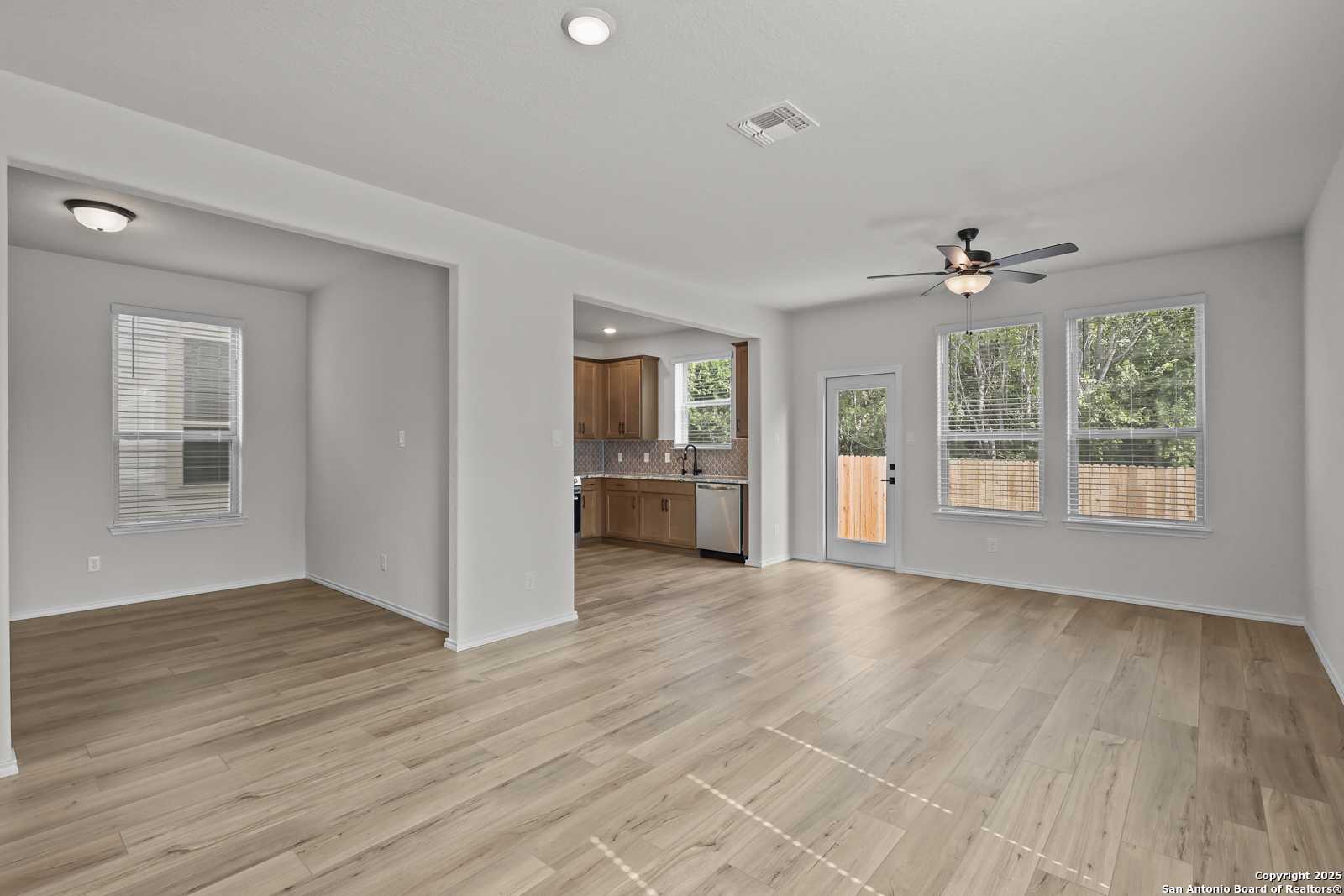 Open-concept living room and kitchen with hardwood floors, white cabinets, and sliding door to backyard in The Florence C, Cedar Heights, San Antonio