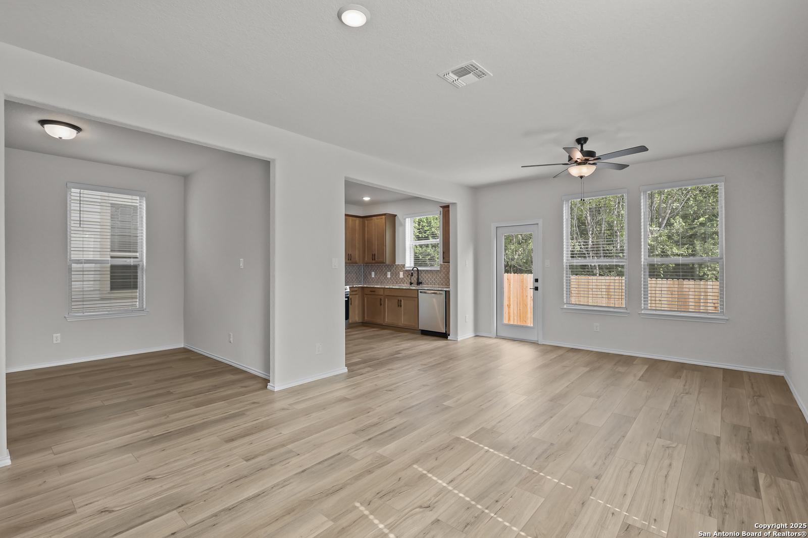 Open-concept living room and kitchen with hardwood floors, white cabinets, and sliding door to backyard in The Florence C, Cedar Heights, San Antonio