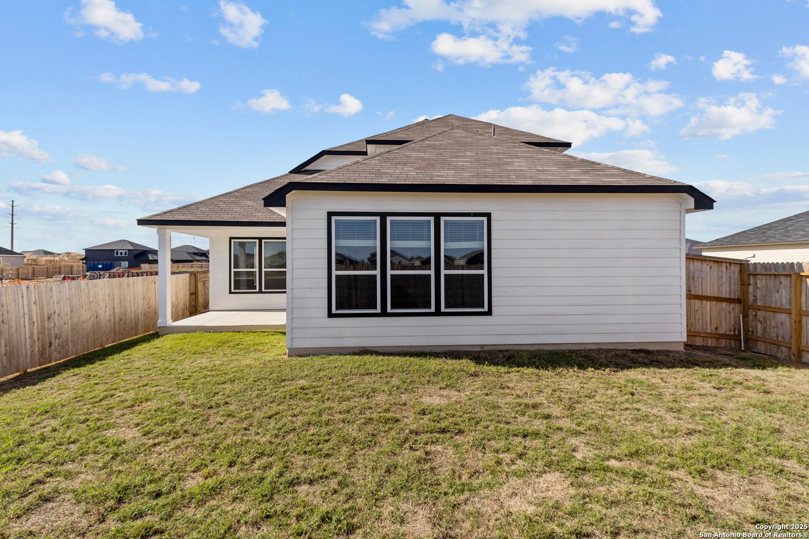 Covered back patio with black-framed windows on white single-story home, fenced grassy yard in Hannah Heights, Seguin, Texas - The Collin B by Davidson Homes
