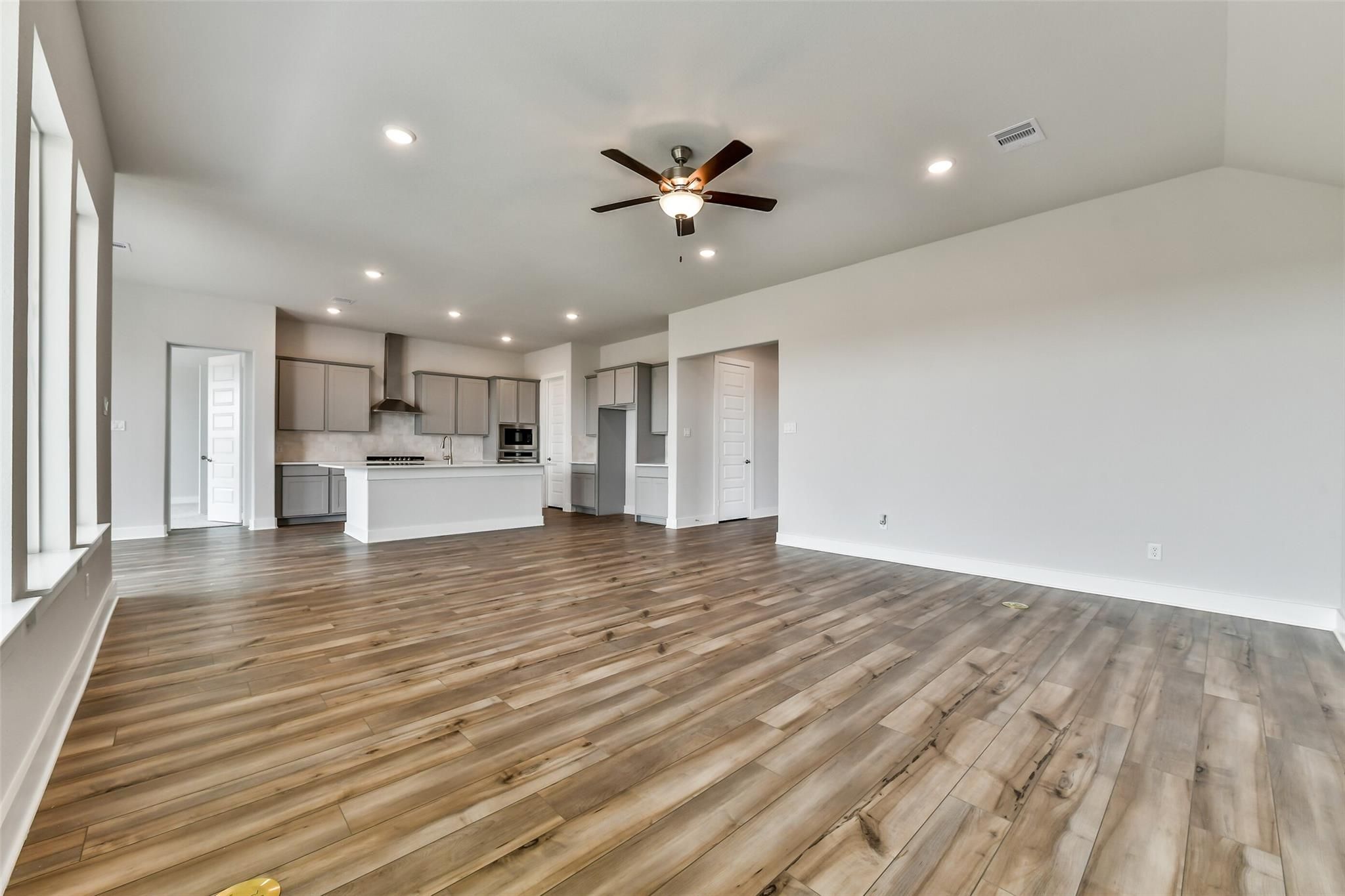 Open-concept living room with hardwood floors, white cabinets, and ceiling fan in Davidson Homes The George A, Lago Mar, Texas City