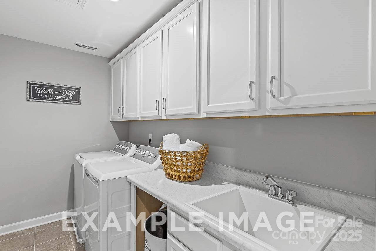Bright laundry room with white cabinets, washer, dryer, utility sink and towel basket in Davidson Homes The Hemlock A, Belmont, NC