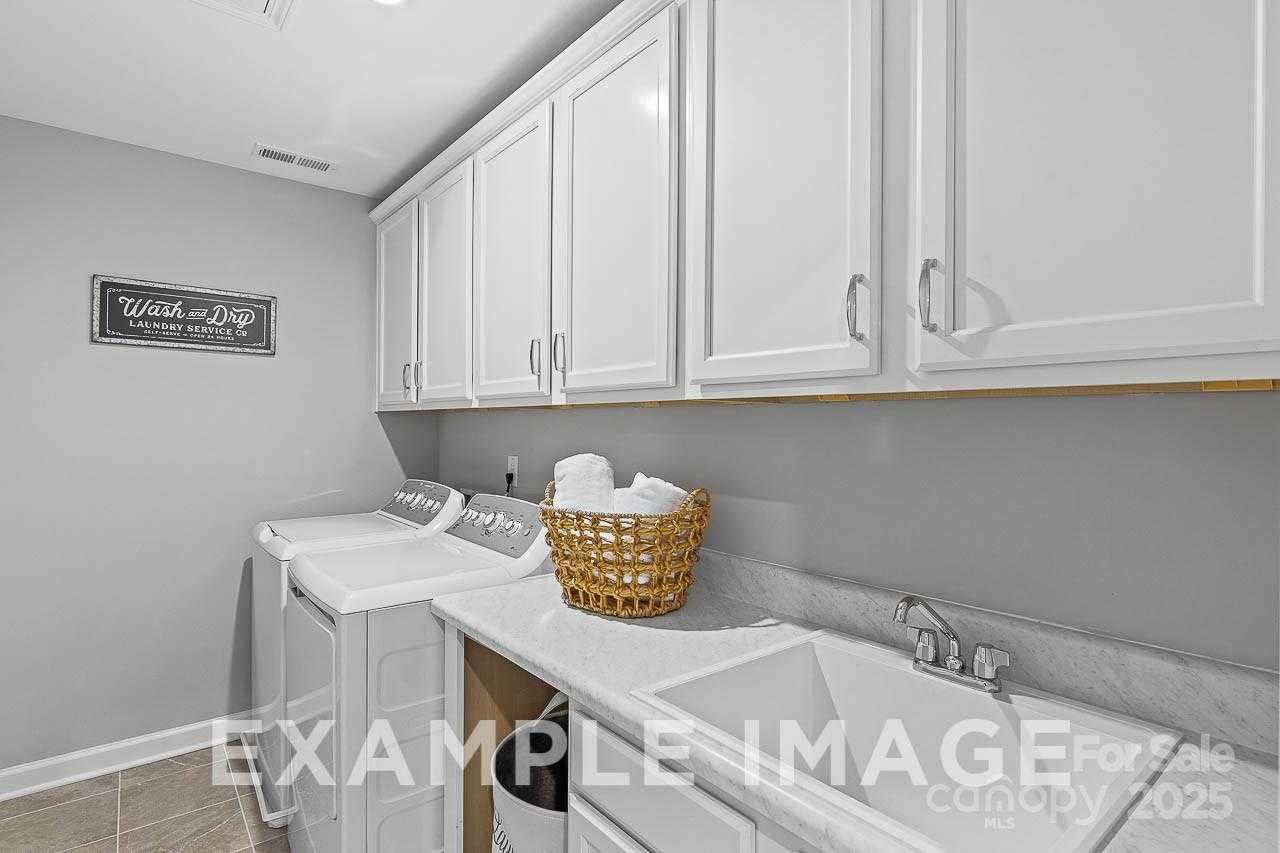 Bright laundry room featuring white cabinets, washer, dryer, utility sink and basket in Davidson Homes The Hemlock A, Enclave at Belmont, NC