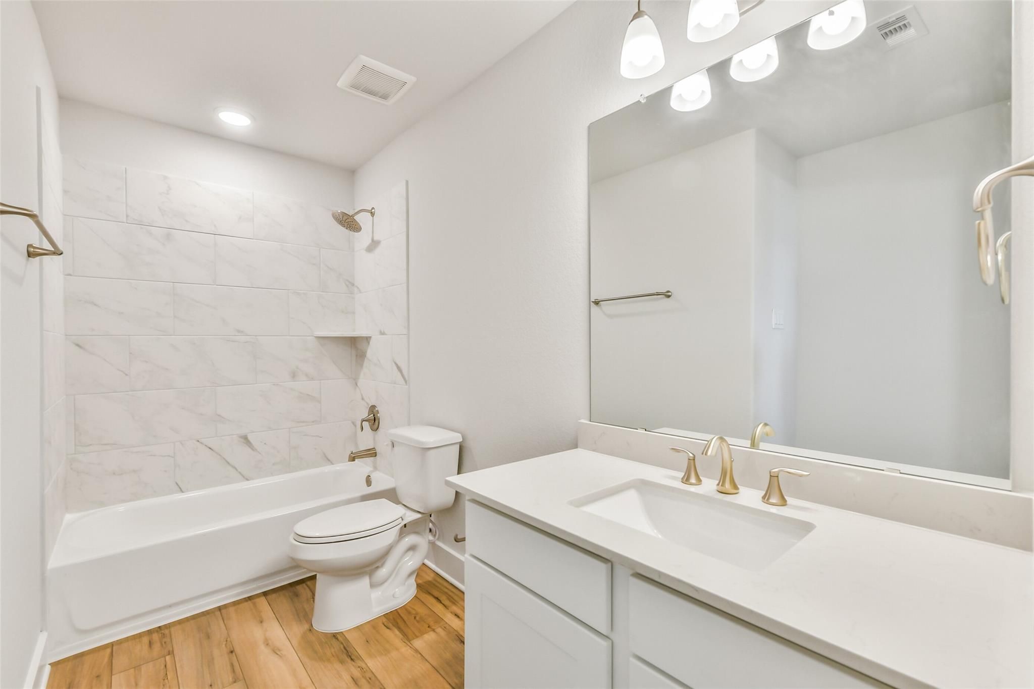 Elegant white bathroom with marble tile shower-tub combo, quartz vanity, gold fixtures in Davidson Homes The Victoria A, Lago Mar, Texas
