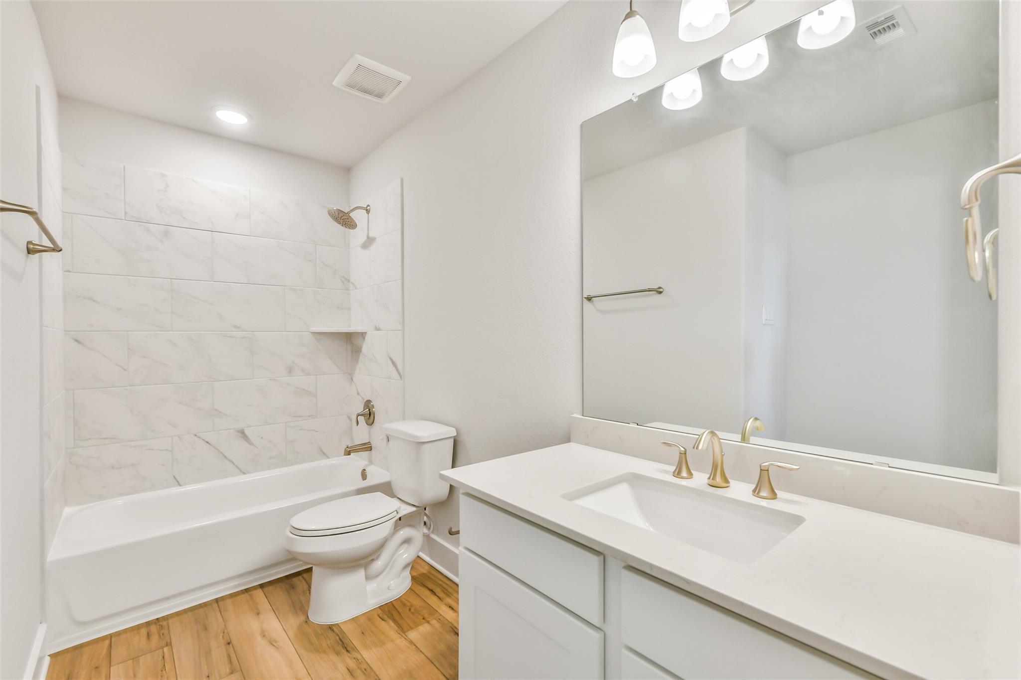 Elegant white bathroom with marble tile shower-tub combo, quartz vanity, gold fixtures in Davidson Homes The Victoria A, Lago Mar, Texas