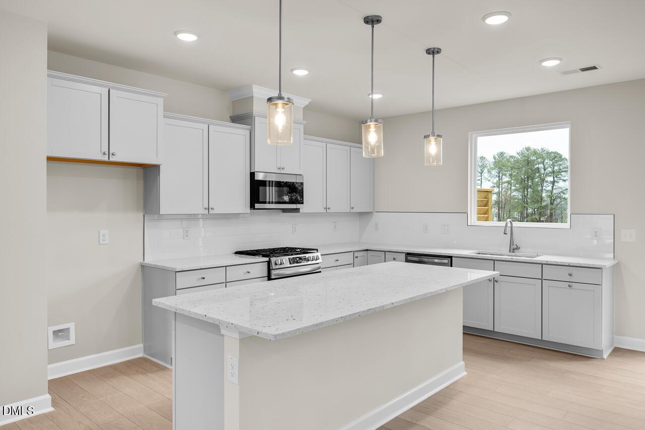 Modern kitchen with white shaker cabinets, quartz island, stainless appliances, and pendant lights in Davidson Homes The Avery, Knightdale, NC
