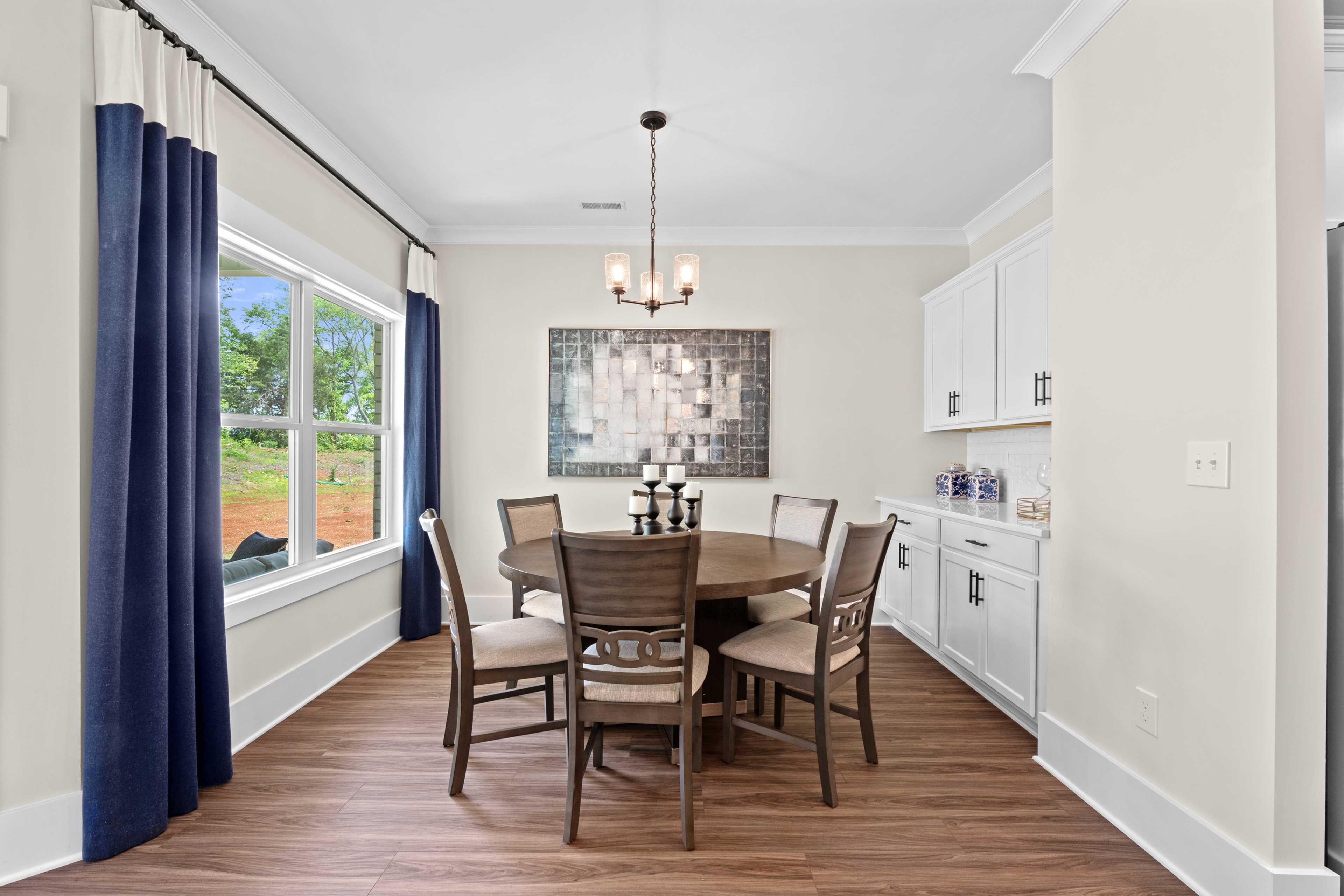 Elegant dining room at Ivy Hills in Toney, Alabama by Davidson Homes featuring round wooden table, blue curtains, abstract art