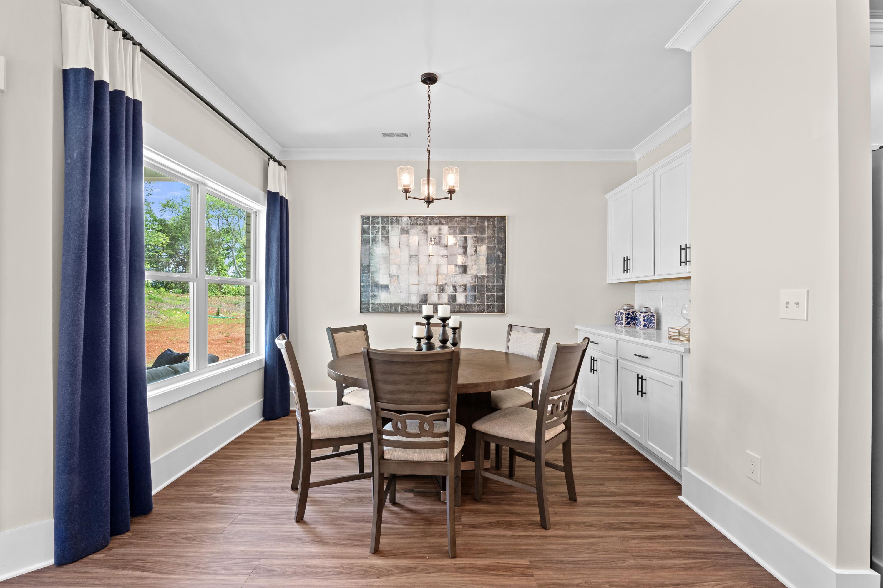 Elegant dining room at Ivy Hills in Toney, Alabama by Davidson Homes featuring round wooden table, blue curtains, abstract art