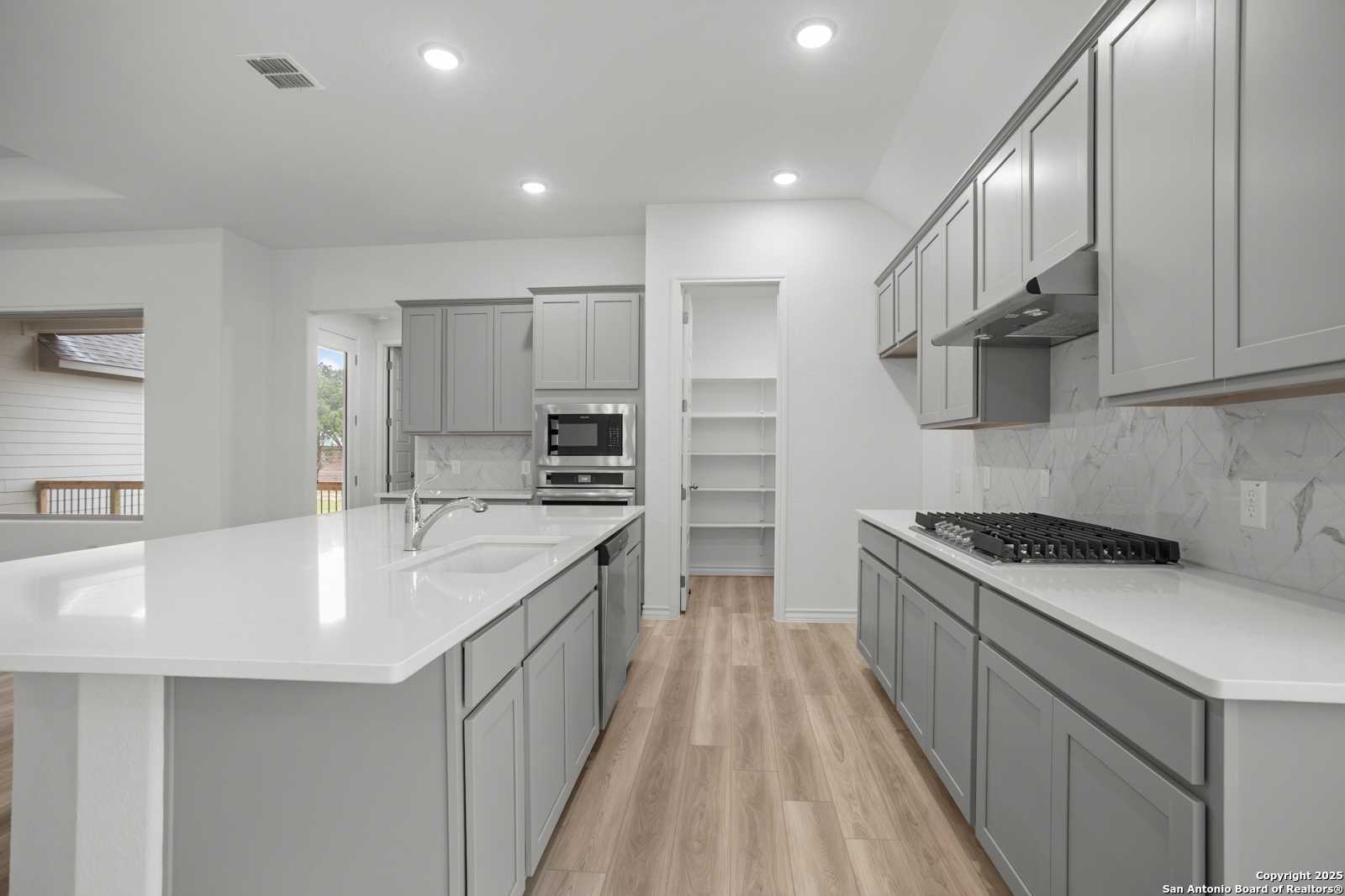 Modern gray shaker kitchen with white quartz island, stainless gas range, walk-in pantry in Davidson Homes Summerlin B, Castroville TX