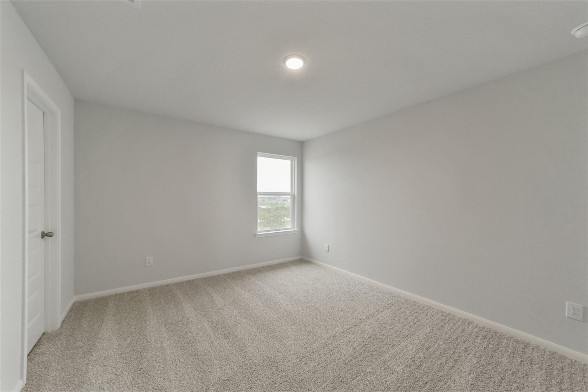 Bright empty secondary bedroom with light gray walls, beige carpet, and window in Davidson Homes The San Marcos E, Beasley Texas
