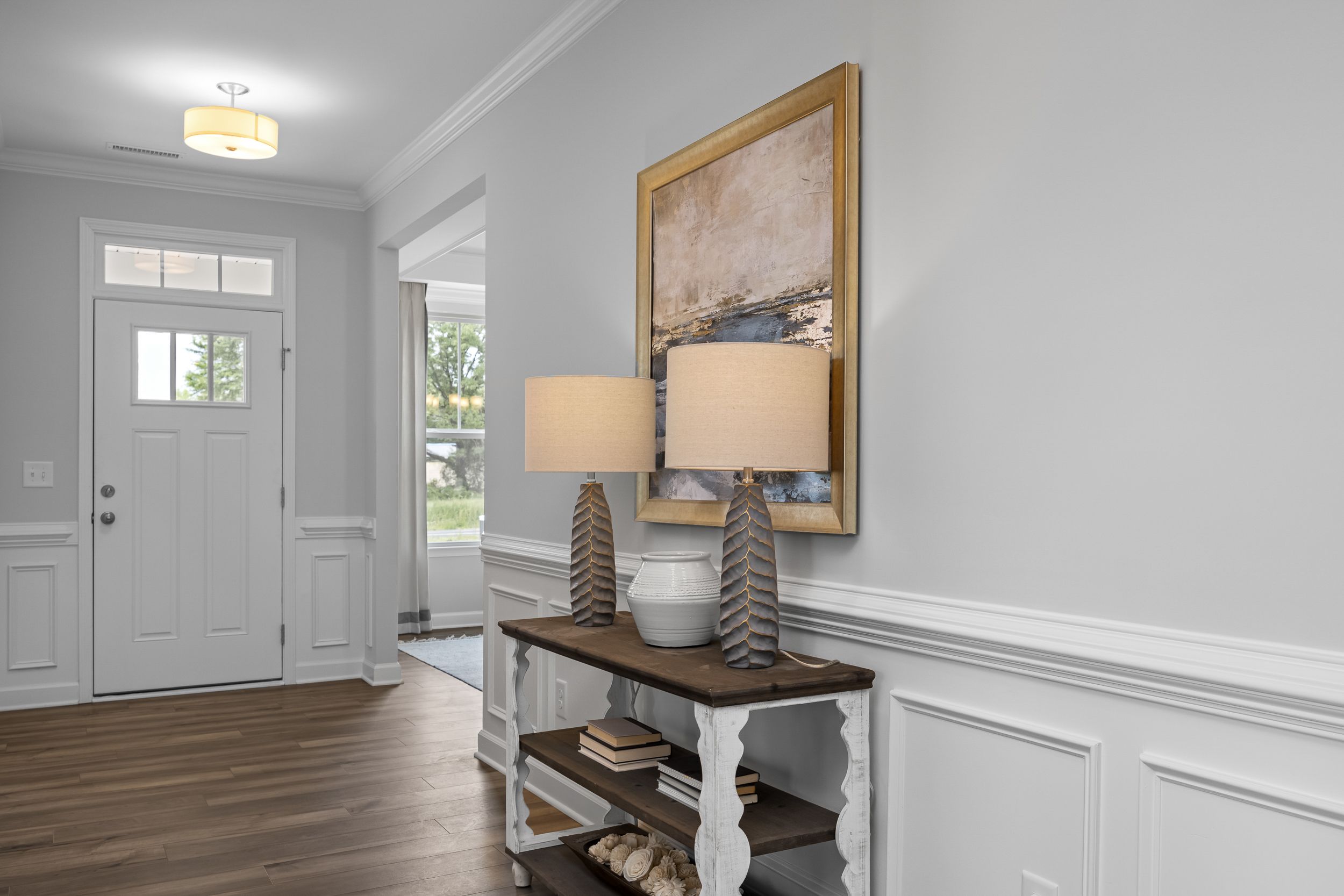 Spacious entryway in The Magnolia D with hardwood floors, gray walls, console table, lamps, and abstract art