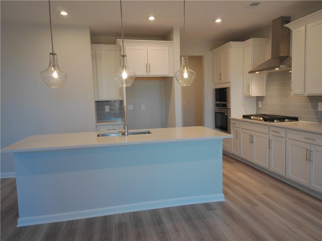 Modern white kitchen island with sink, stainless range, and pendant lights in Davidson Homes The Marion C, Winder, Georgia